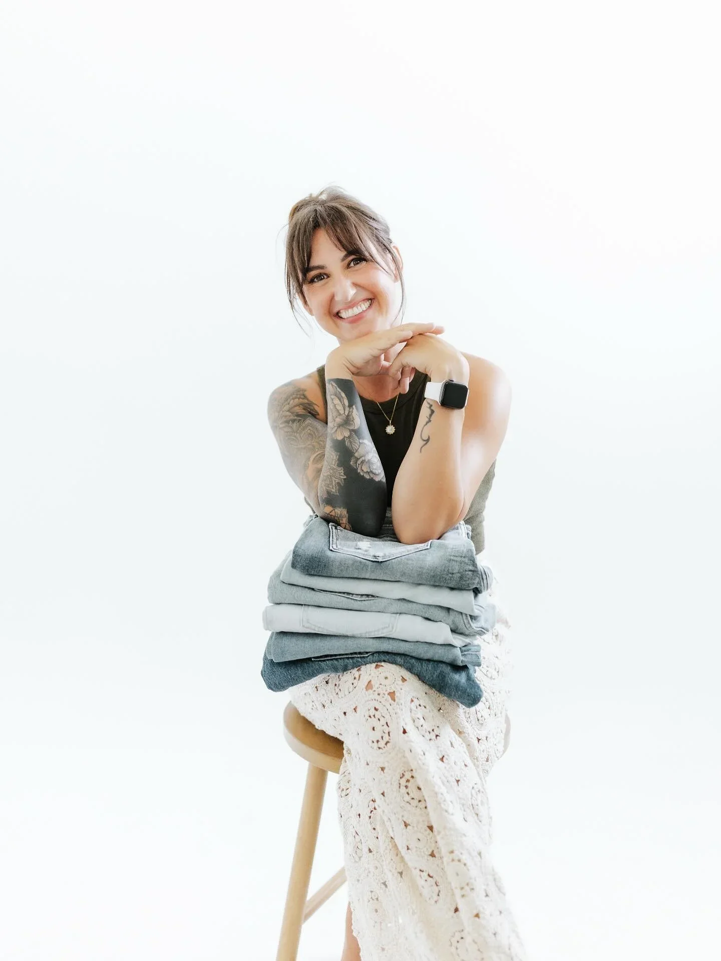 Terrin Marino, founder of Saucha Living in Fayetteville, NC, smiling with a stack of perfectly folded jeans to demonstrate wardrobe organization.