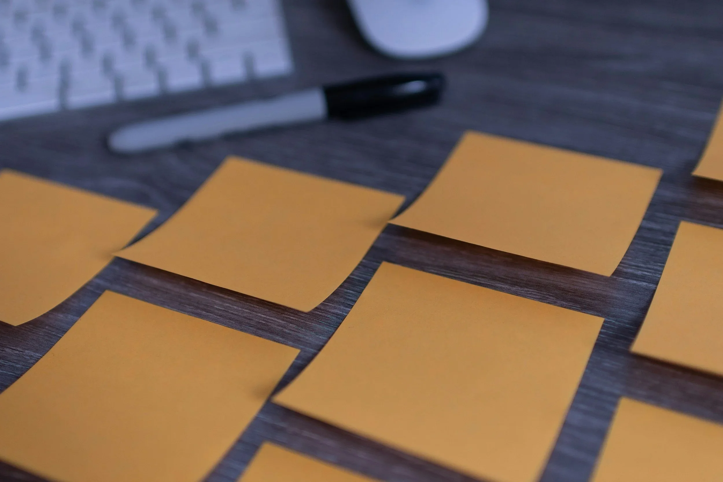 Close-up of yellow sticky notes arranged on a wooden desk with a marker and keyboard in the background for office organization.
