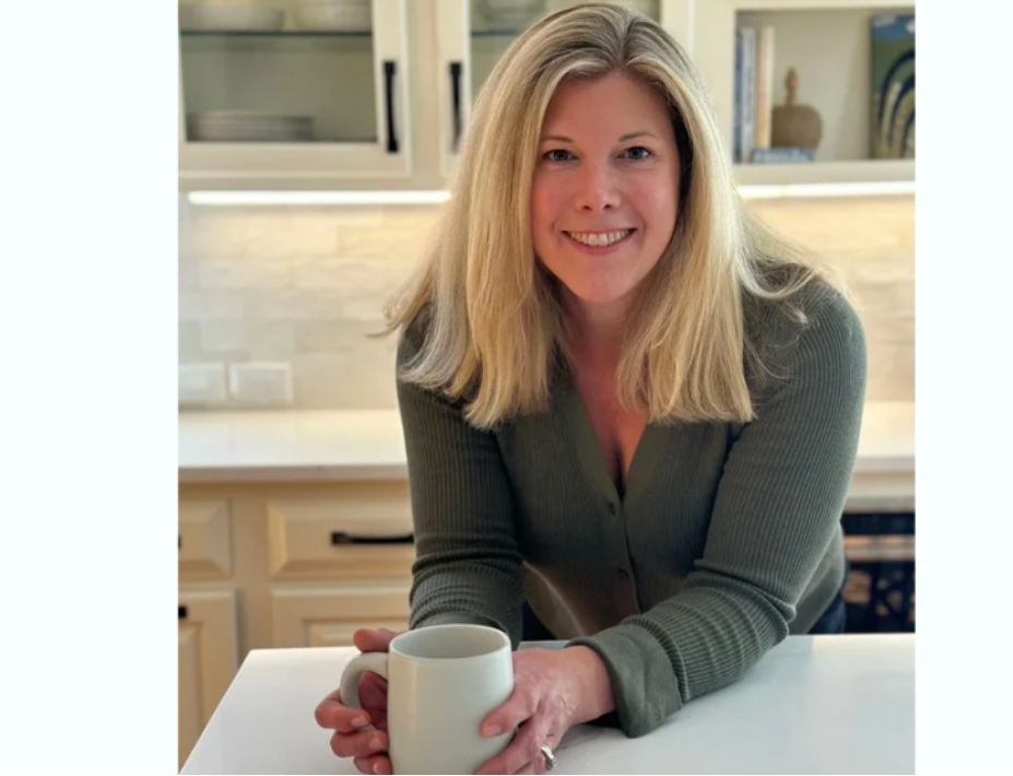 Holly Gray, founder of Holly’s In The House professional organizing, smiling in a modern kitchen while holding a white coffee mug.
