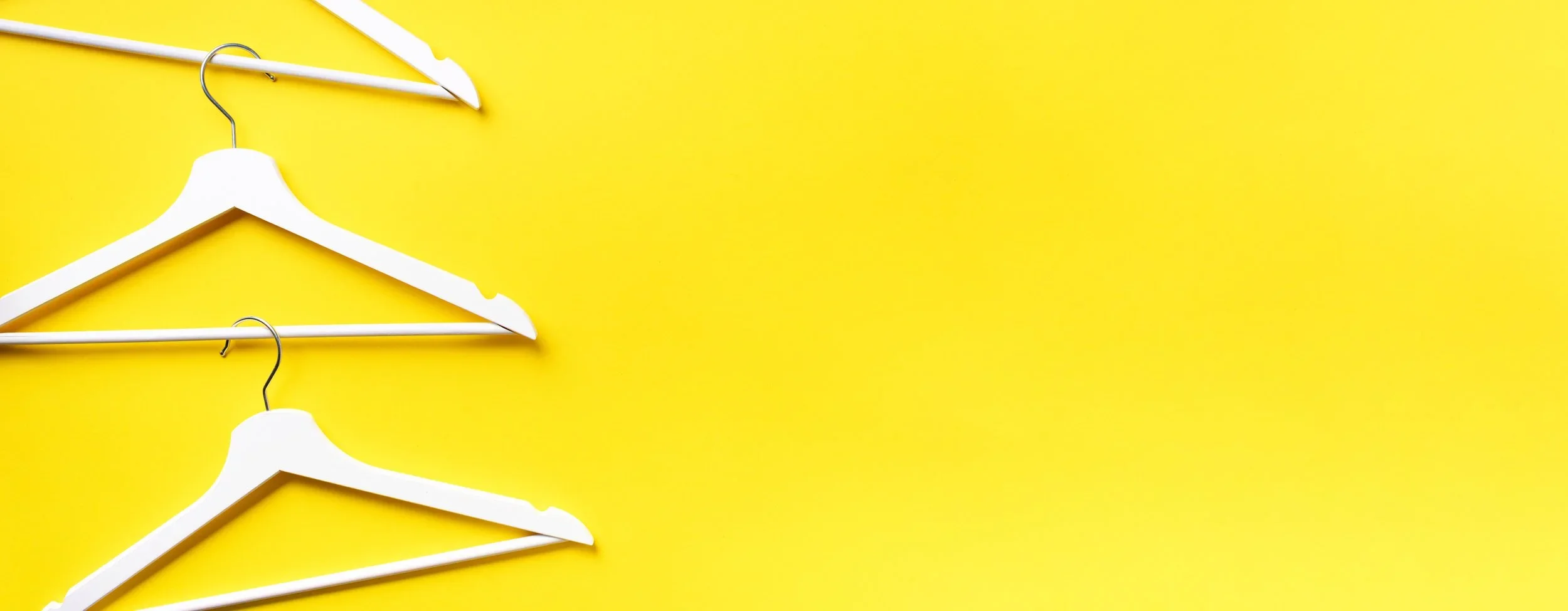 Minimalist white wooden clothes hangers arranged on a bright yellow background by Pro Organizer Studio.