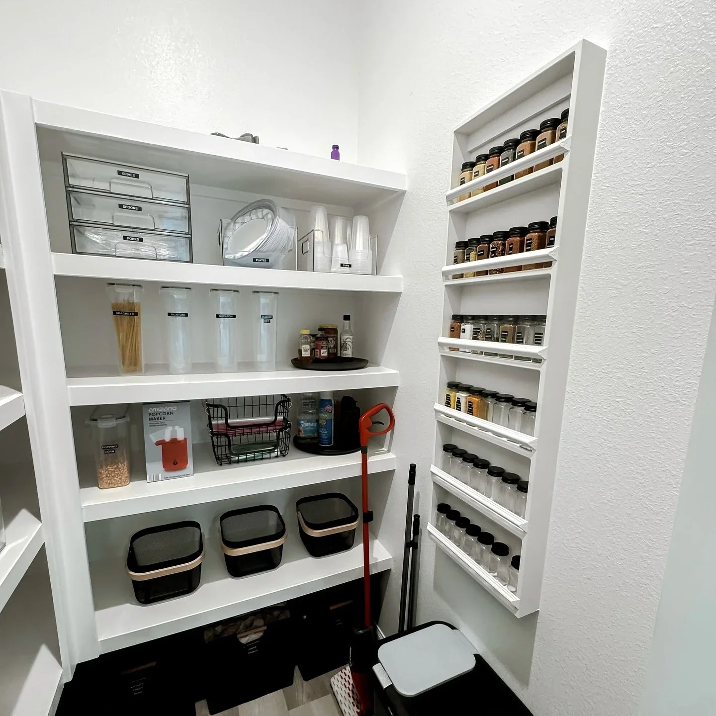 A white walk-in pantry by Organized by Onyee with a wall-mounted spice rack and clear storage containers.