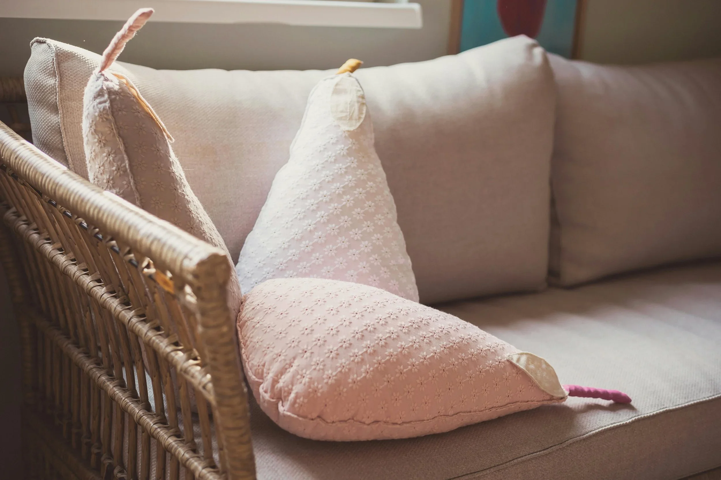 Soft pink pear-shaped pillows on a wicker sofa in an organized, peaceful nursery.