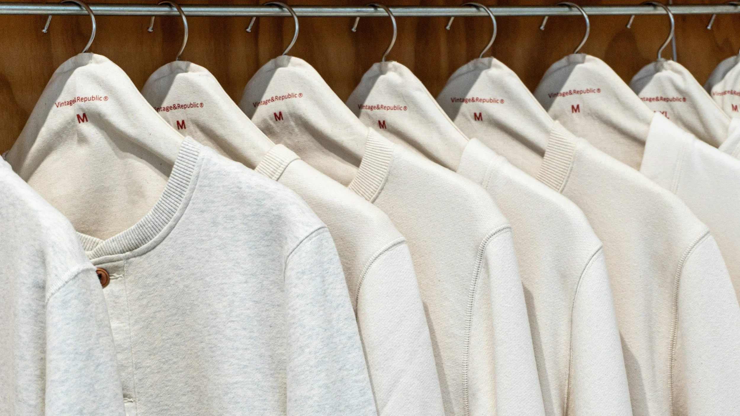 A neat row of cream Vintage & Republic sweaters hanging on a closet rod, demonstrating professional wardrobe organization by Sweet Spaces in NJ.