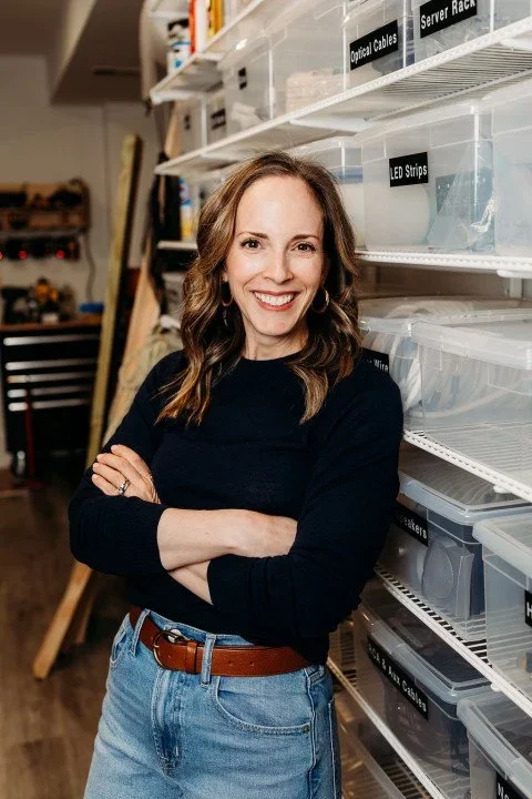 Christy, professional organizer, smiling in front of a shelf of labeled storage bins.