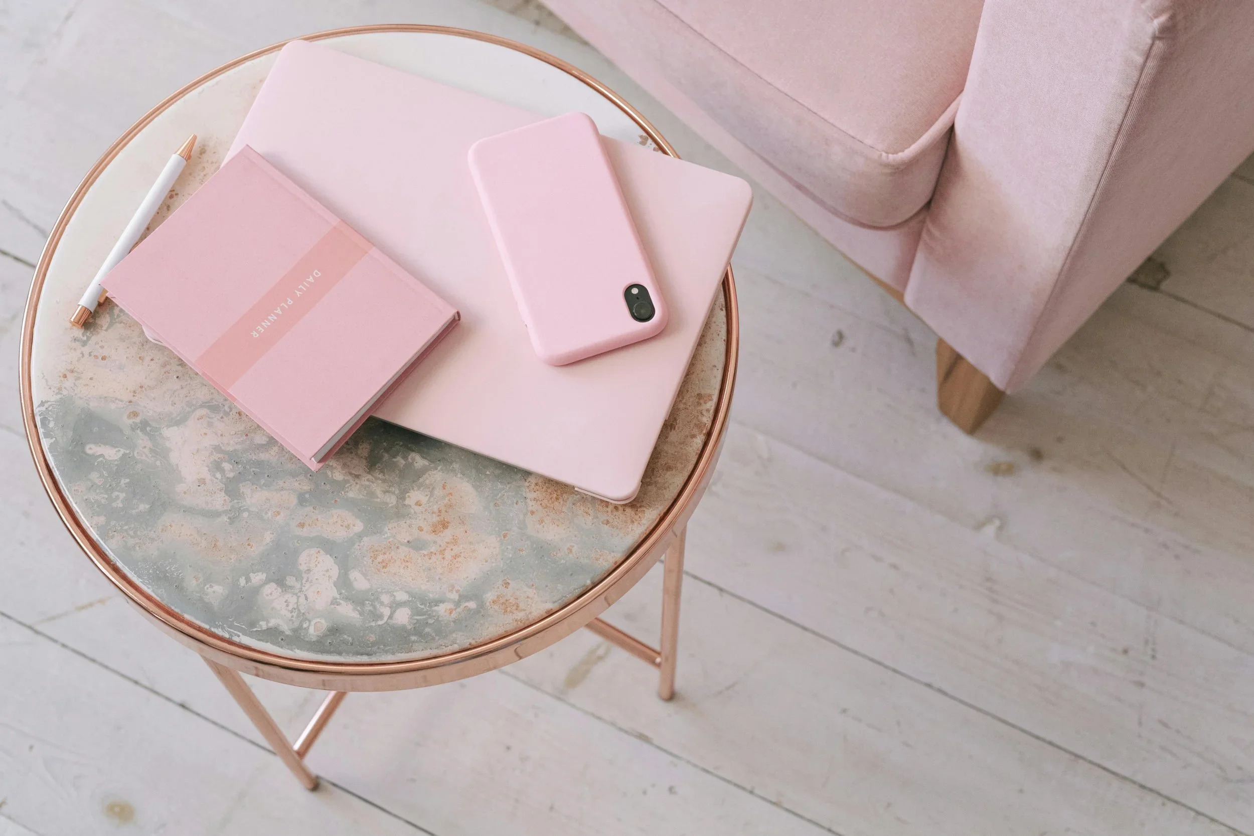 Pink laptop, phone, and planner on a marble side table in an organized home office.