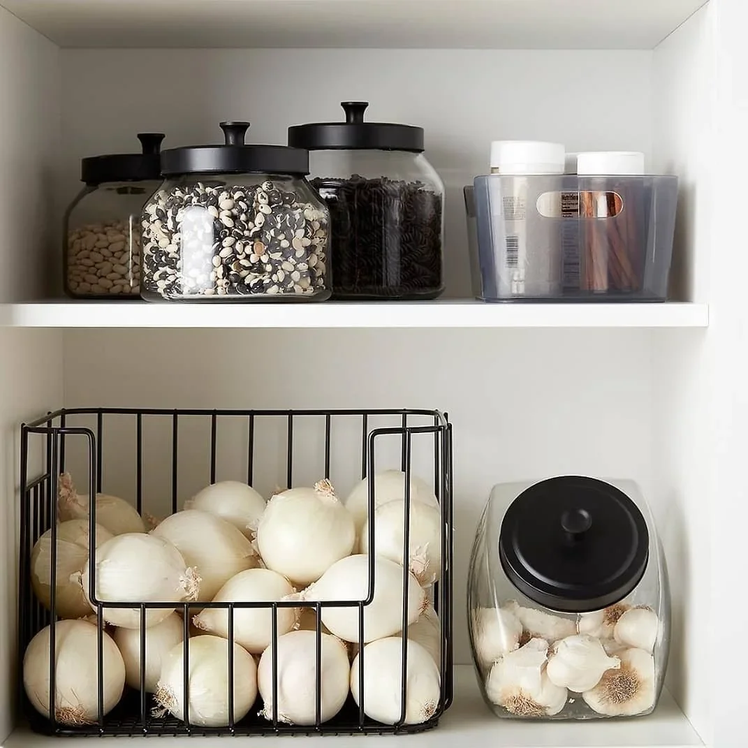 Professional pantry organization by Michele Makes Space in Columbus, featuring white onions in a black wire basket and garlic in a glass jar with a matte black lid.