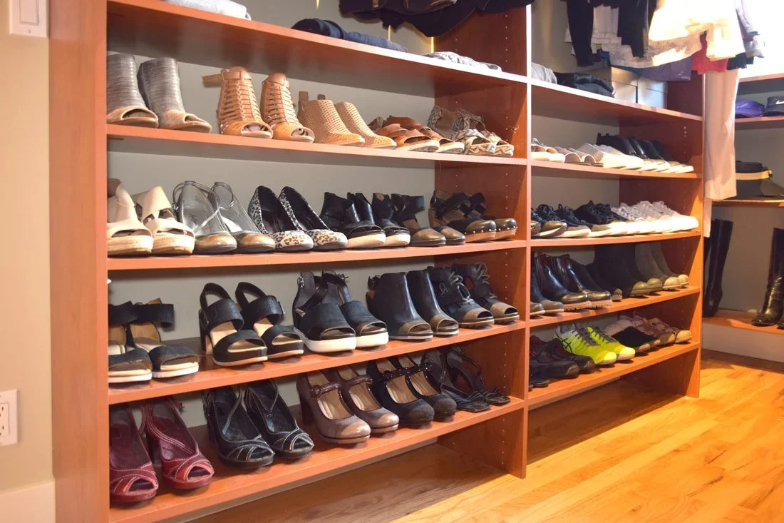 Neatly organized rows of women's shoes on wood shelving in a walk-in closet.