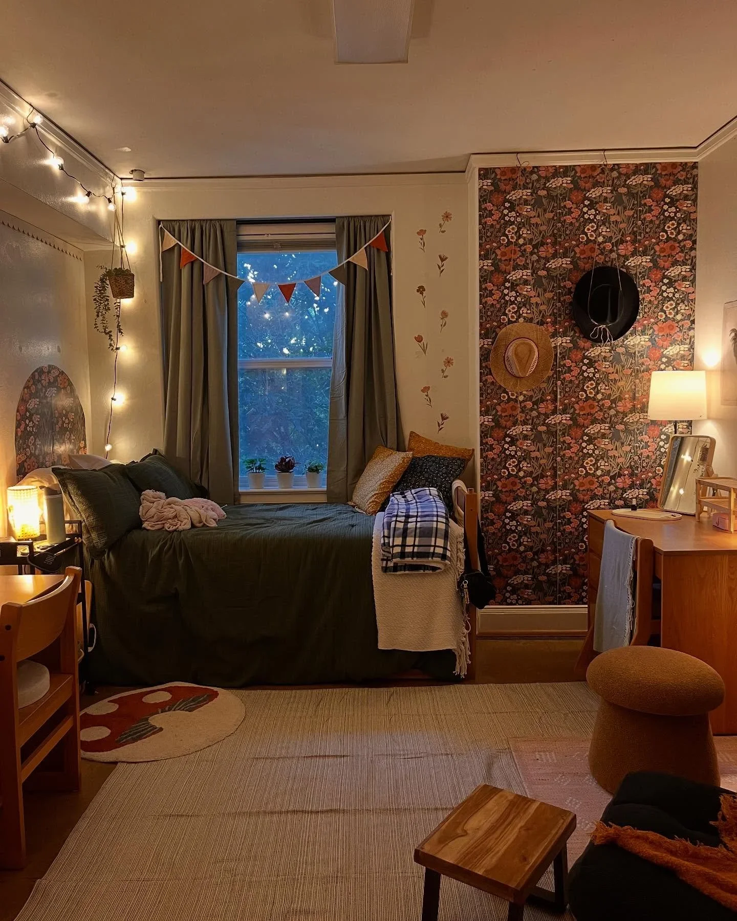 Cozy bedroom by A Neat Day featuring a dark green bed, floral wallpaper, fairy lights, and a small desk.