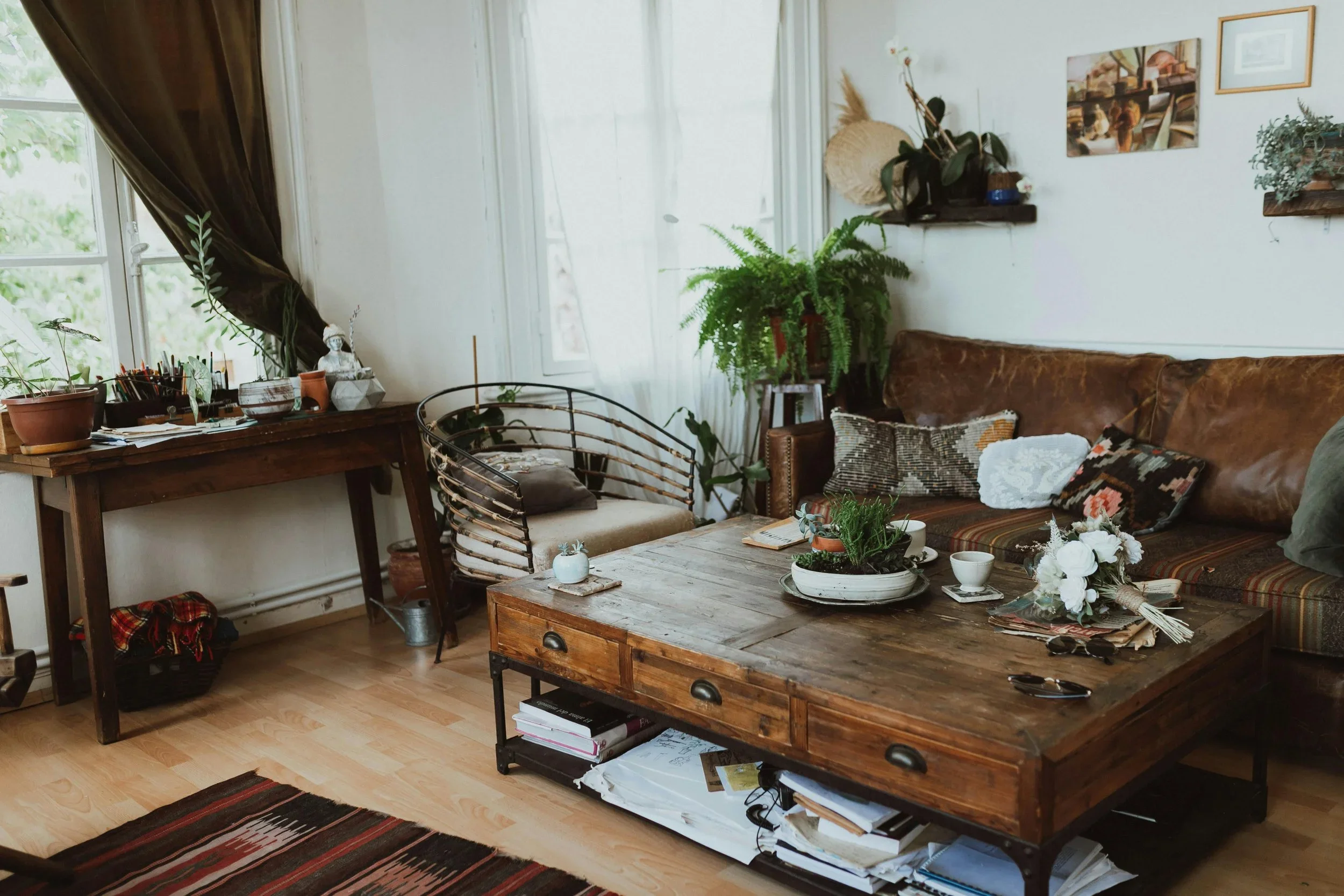 Eclectic living room with a large wooden coffee table, leather sofa, and green houseplants.
