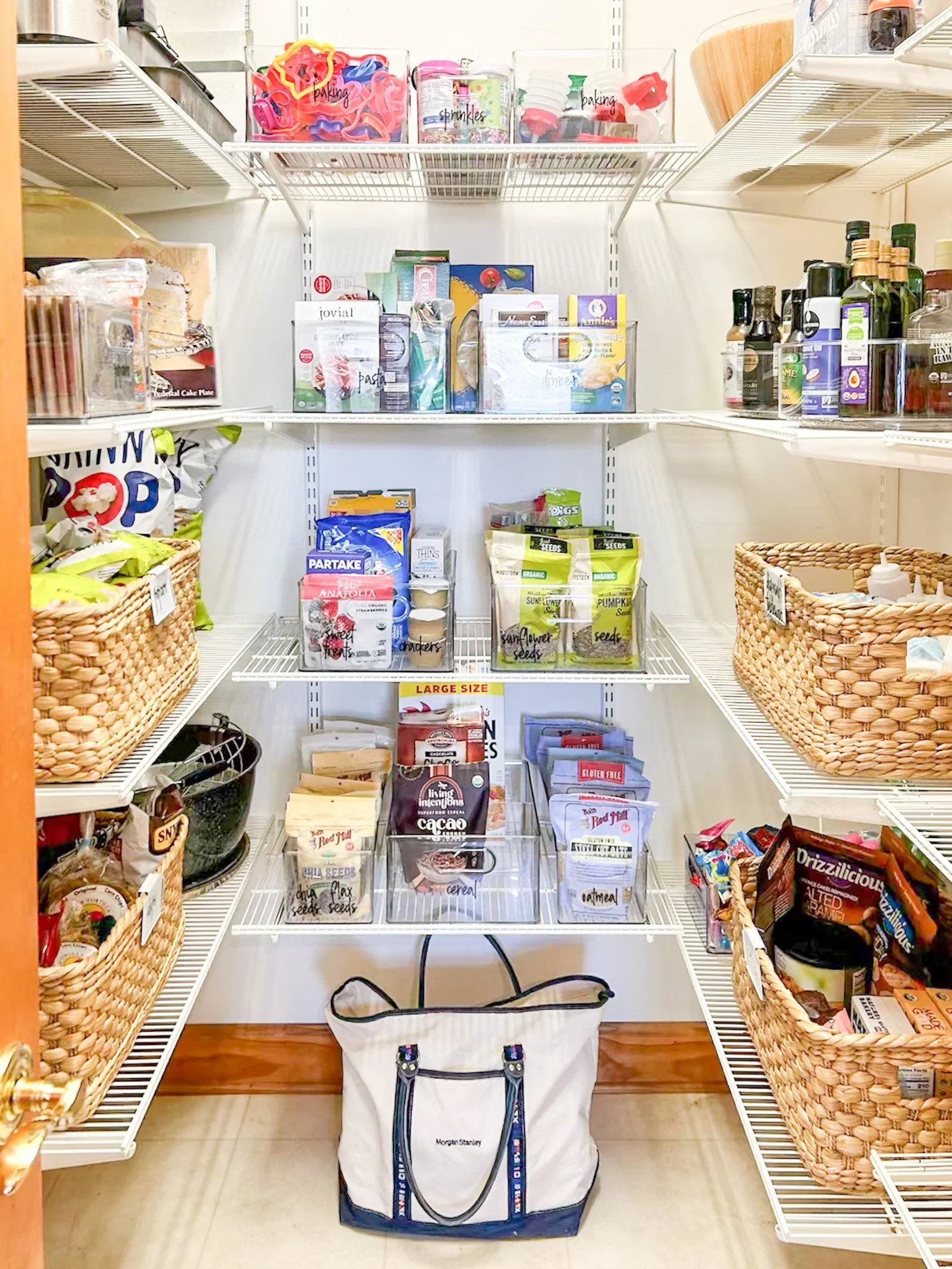 Professionally organized pantry featuring white wire shelving, woven baskets, and labeled clear bins.