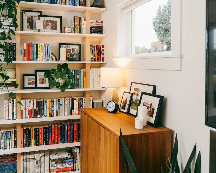 A serene home library organized by Refine Organizing in Seattle, featuring light wood shelves filled with books, framed photos, and a green Pilea plant.
