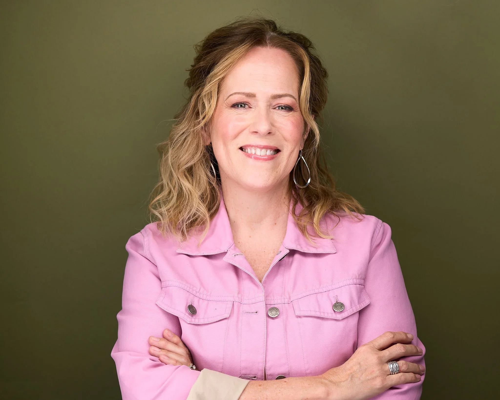 Pinky Jackson, a professional home organizer, smiling in a pink denim jacket against an olive green background.