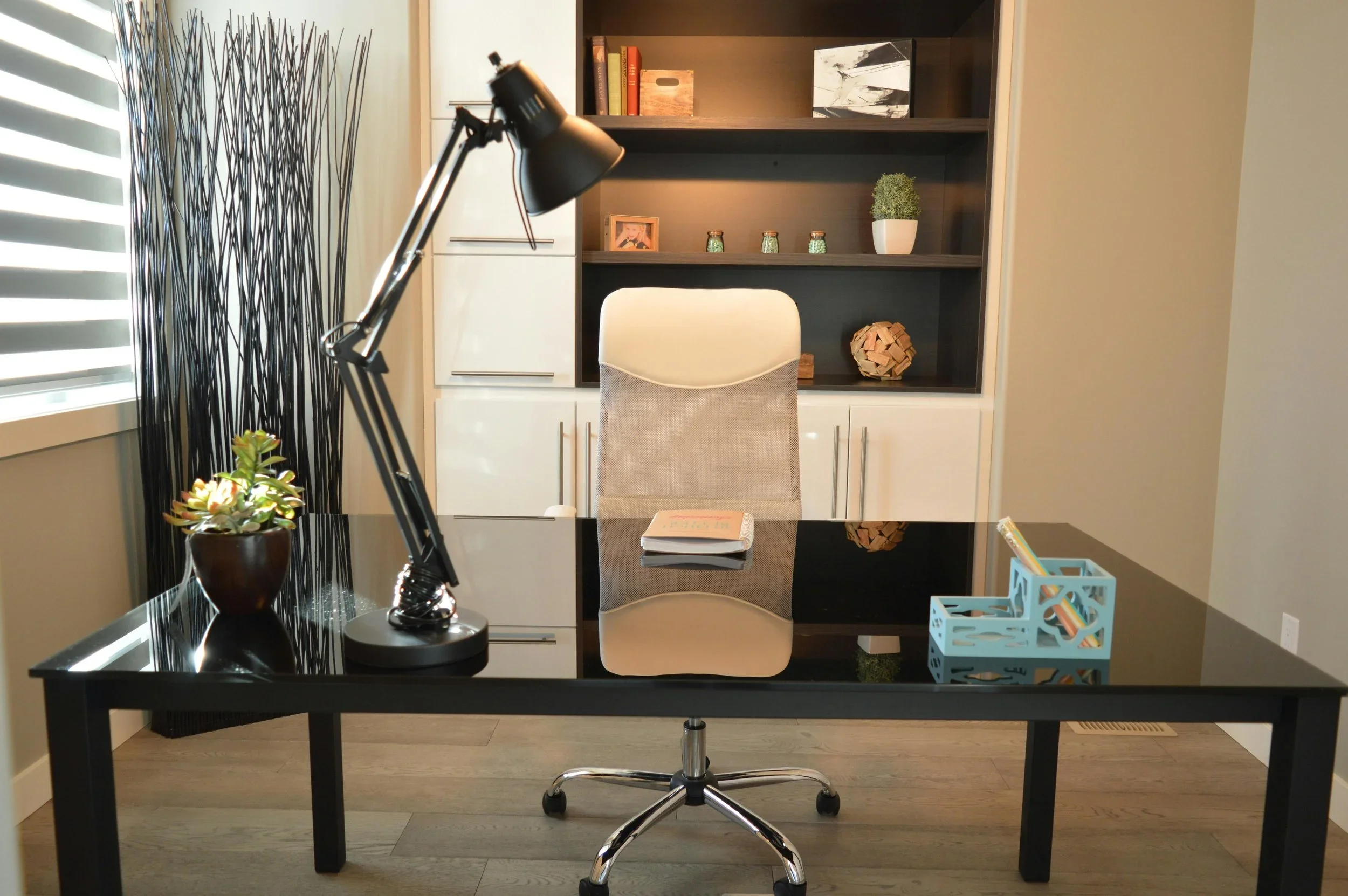A minimalist home office organized by Home By Eleven in Minneapolis, featuring a black glass desk with a task lamp and a white ergonomic chair.