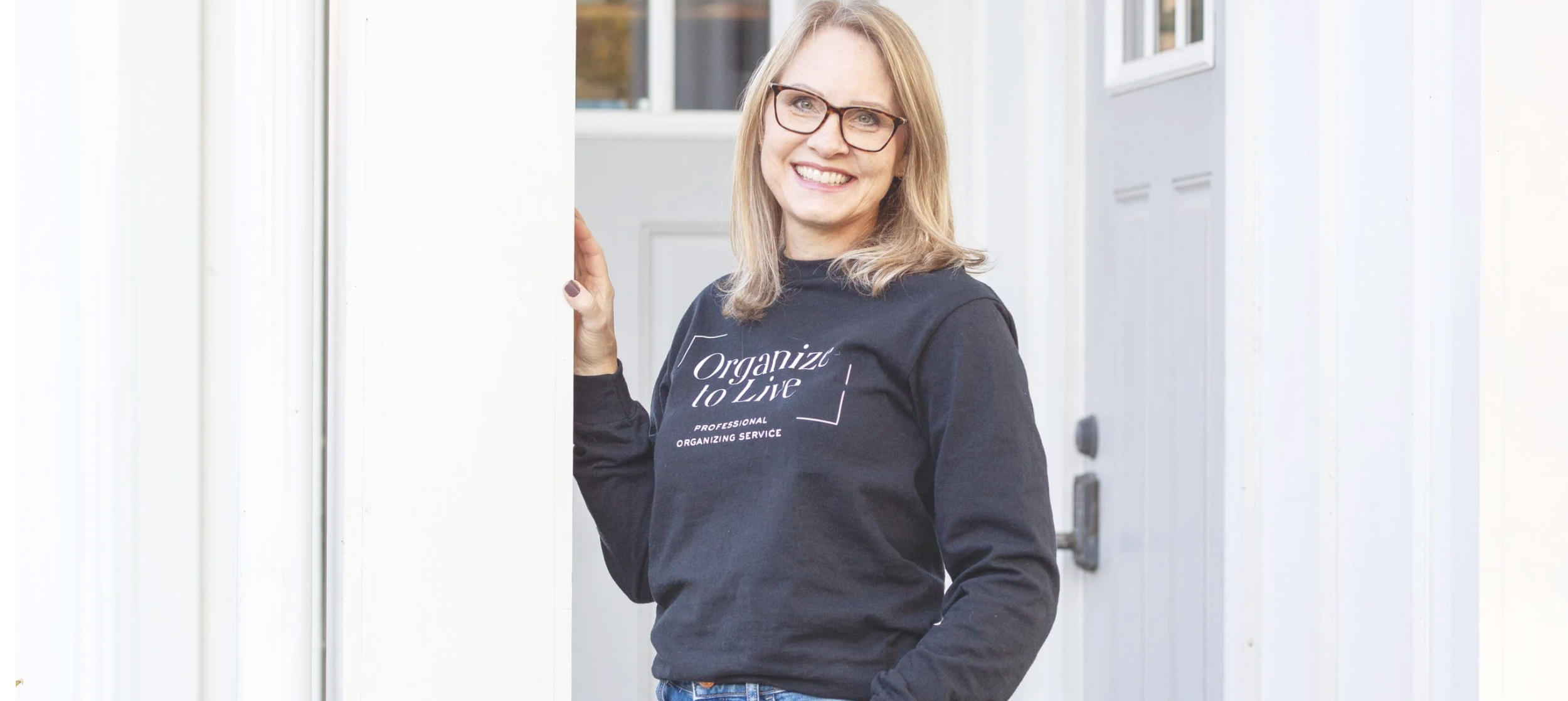Professional home organizer in a branded sweatshirt standing in a bright doorway.