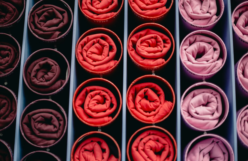 Professional color-coded drawer organization by like BEGETS like, featuring rolled shirts in shades of maroon, red, and pink.