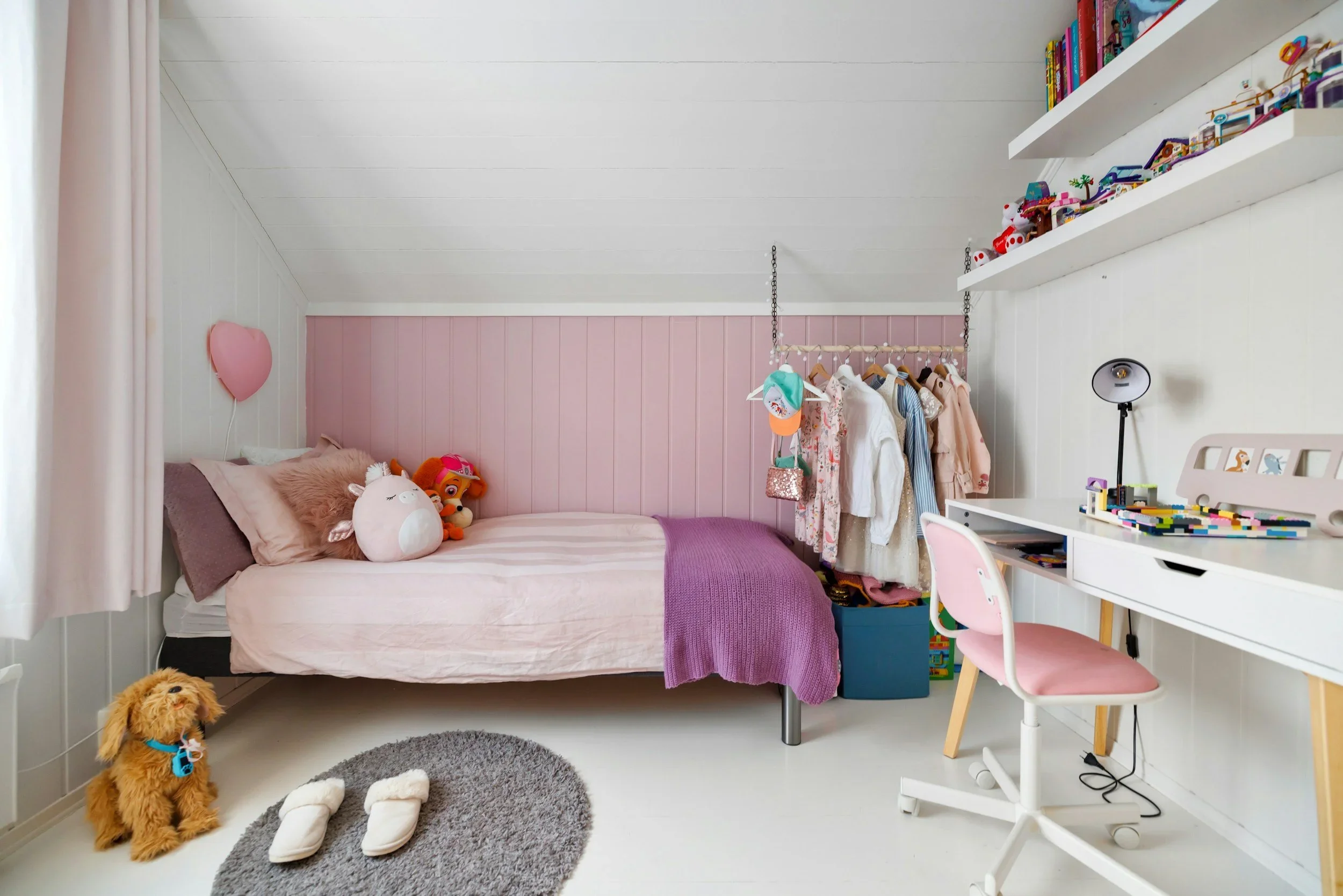 An organized kids' bedroom by Tailored Organizing in Salem, featuring a pink accent wall, white desk, and a neatly arranged hanging clothes rack.