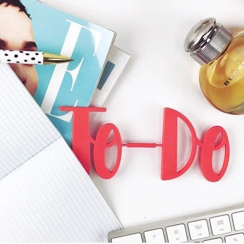 A pink 'To-Do' sign on a white desk with a notebook and pen, representing business systems for organizers.