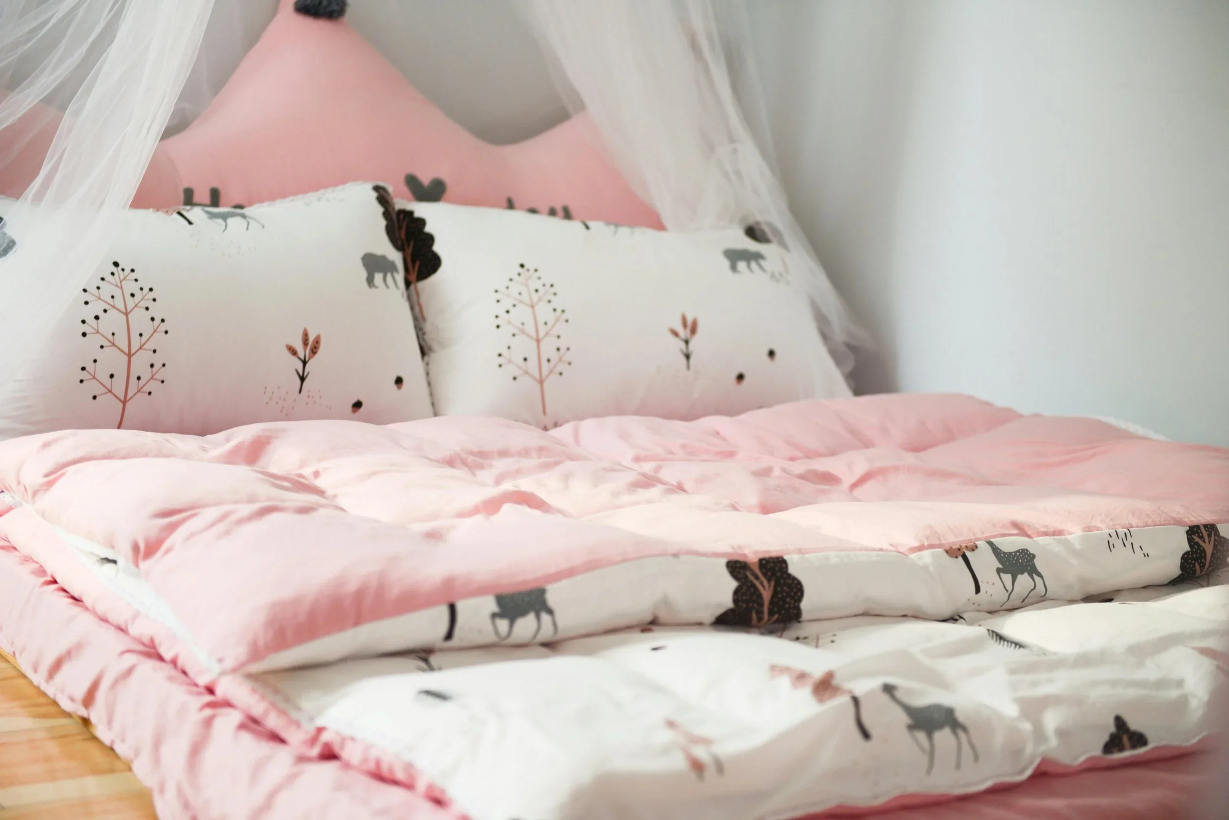 Organized kids bed with pink forest-patterned bedding and tree-shaped pillows.