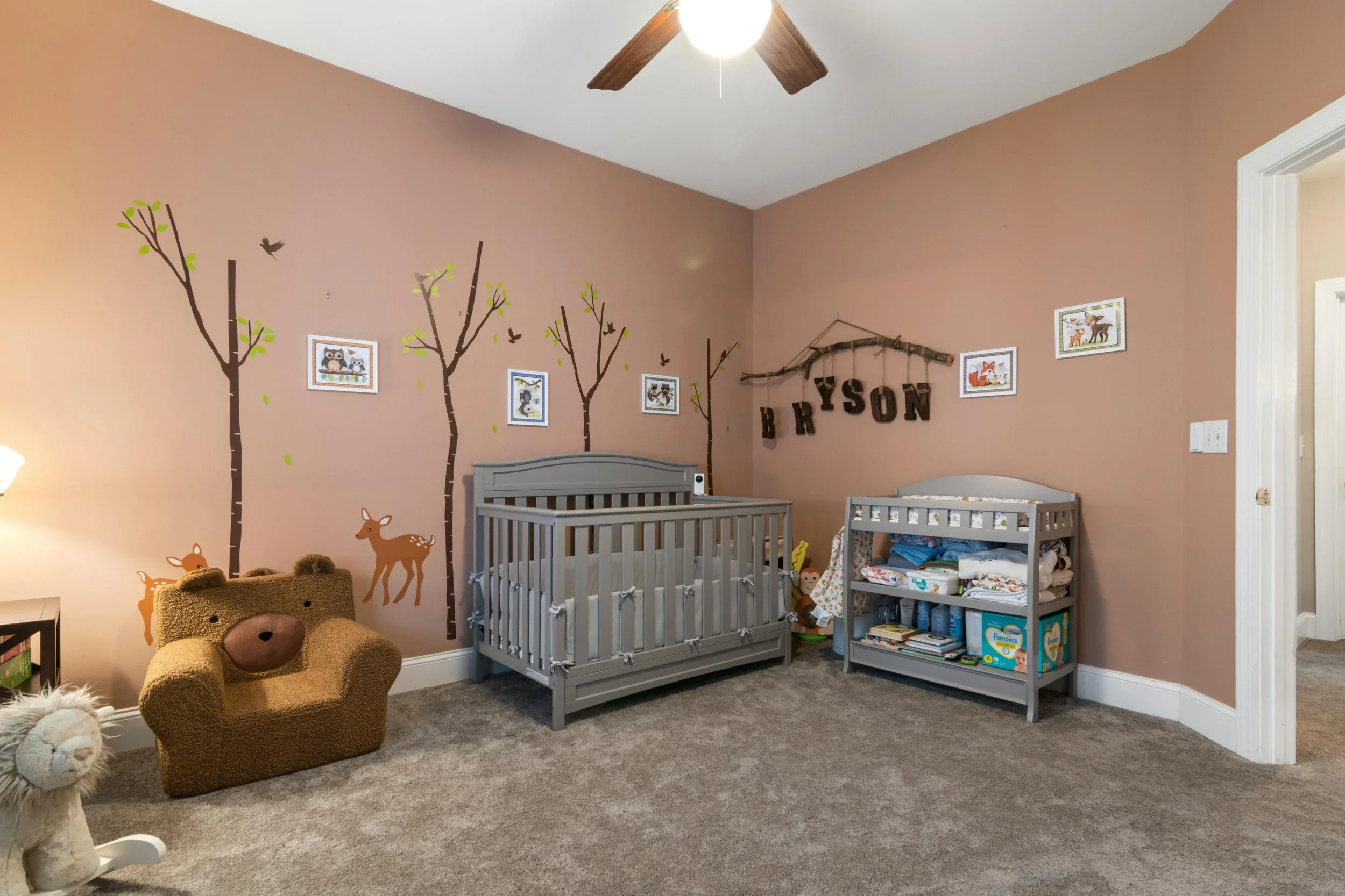 Organized forest-themed nursery with a gray crib, tree wall decals, and a bear-shaped armchair.
