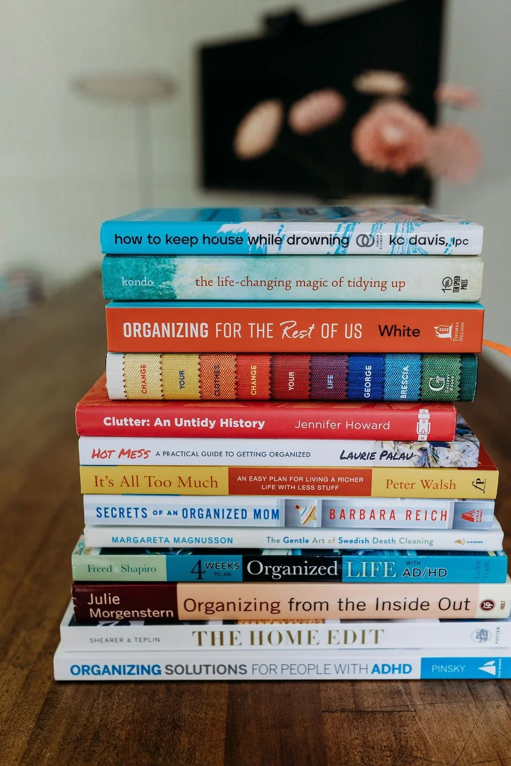 A tall stack of popular home organization and decluttering books on a wooden table.