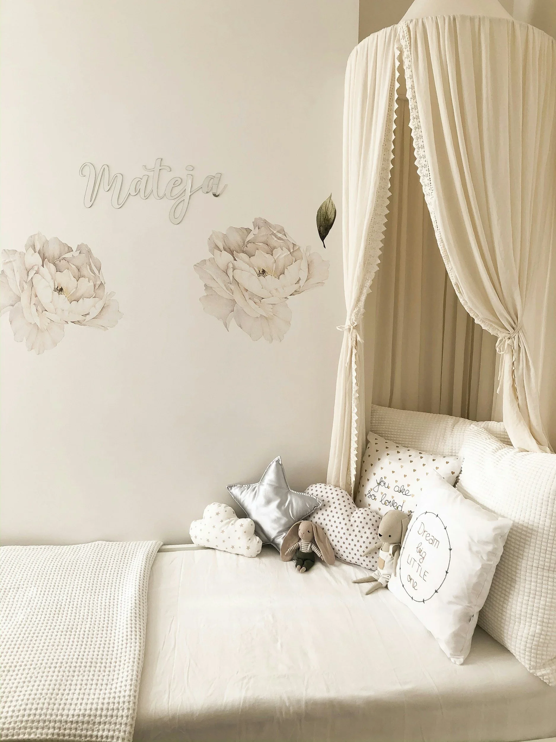 A personalized nursery by The Organized You with floral wall decals, a cream bed canopy, and decorative star and heart pillows.