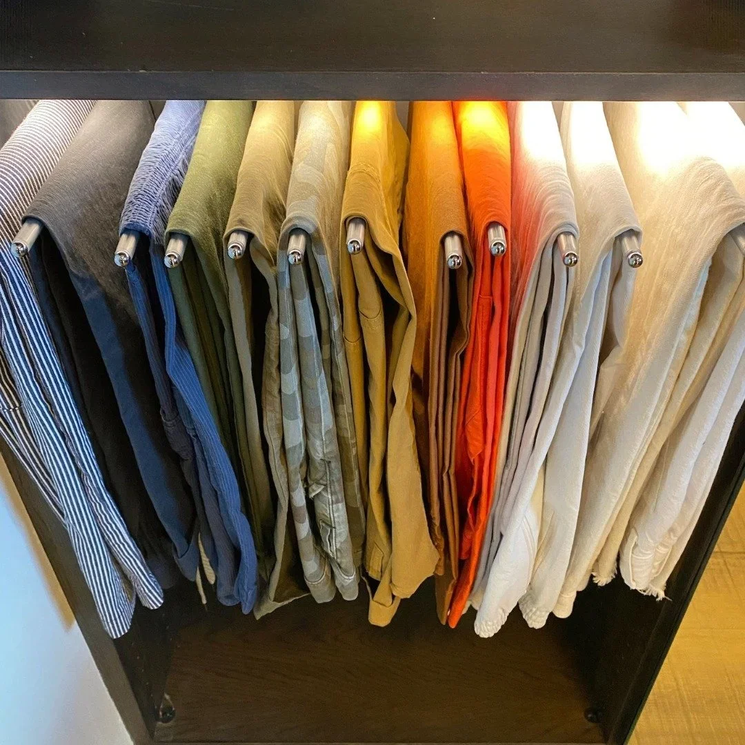 A professional closet organization system by Organized by Keli & Co. in Denver, featuring color-coded trousers hanging on a pull-out rack.