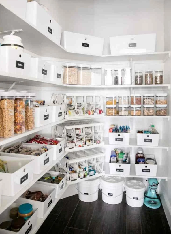 A bright, organized walk-in pantry by We Organize Co. featuring white bins with custom labels and clear airtight food containers.