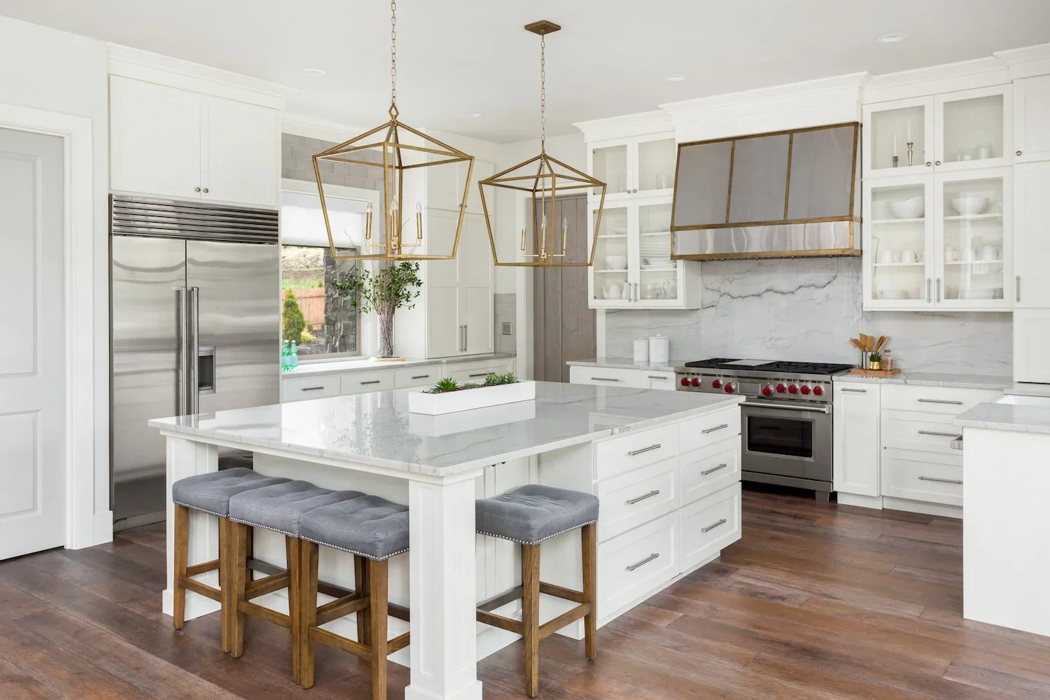 Modern white kitchen with marble countertops and an organized island featuring grey barstools.