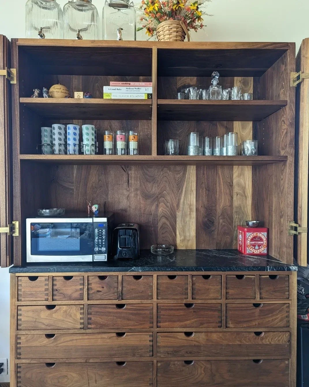 Organized walnut apothecary-style hutch with neatly arranged glassware, books, and a microwave.