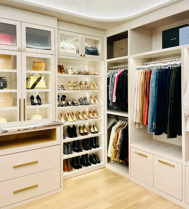 A luxury custom walk-in closet by Incredibly Organized featuring glass cabinets, organized shoe shelves, and color-coordinated hanging clothes.