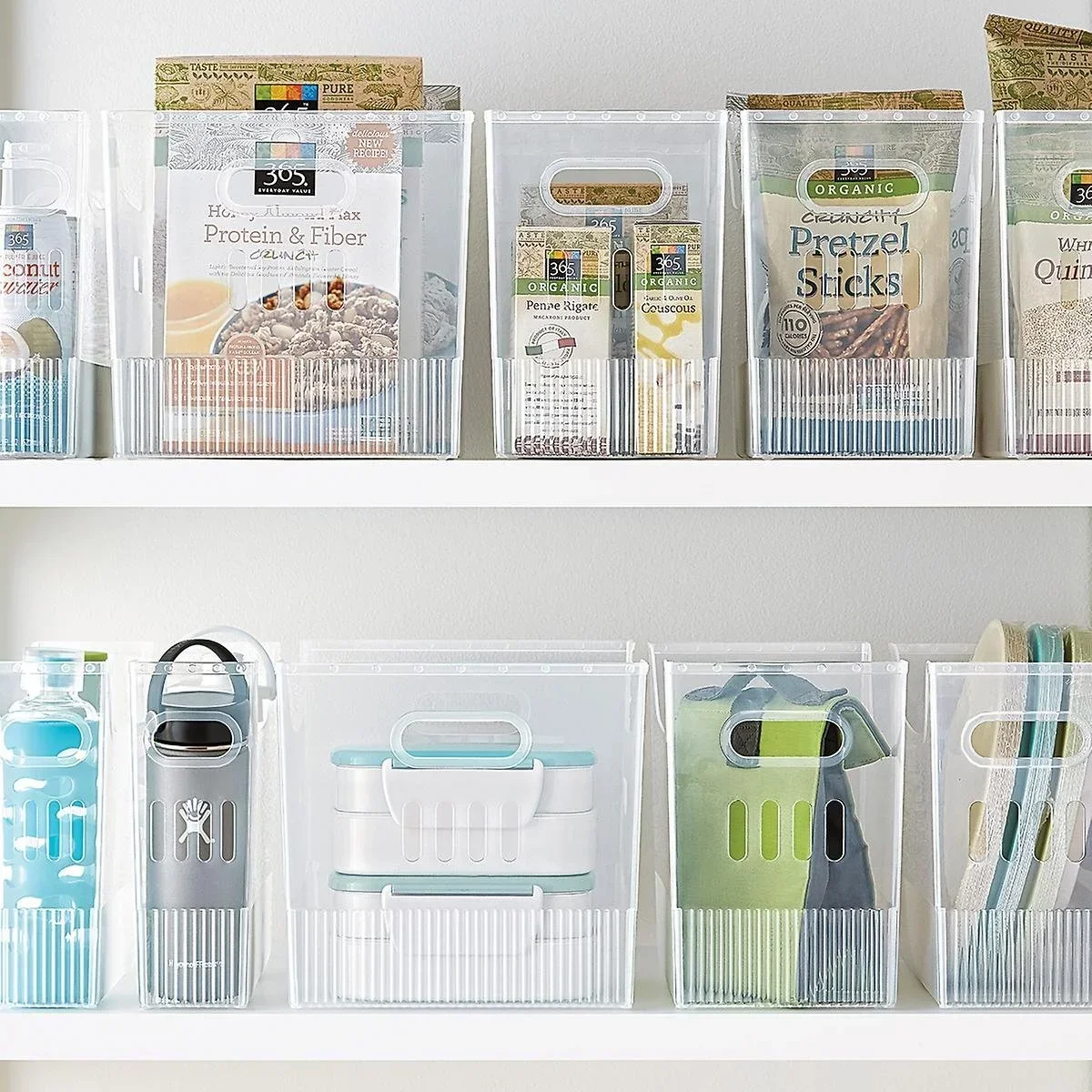 Clear plastic multi-purpose bins organizing snacks and water bottles on white pantry shelves.