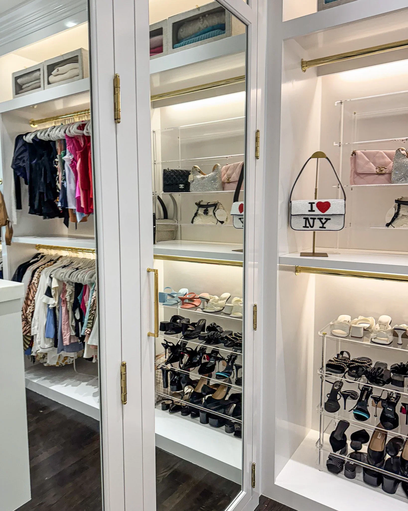Luxury white walk-in closet featuring organized designer handbags, shoes, and mirrored doors.
