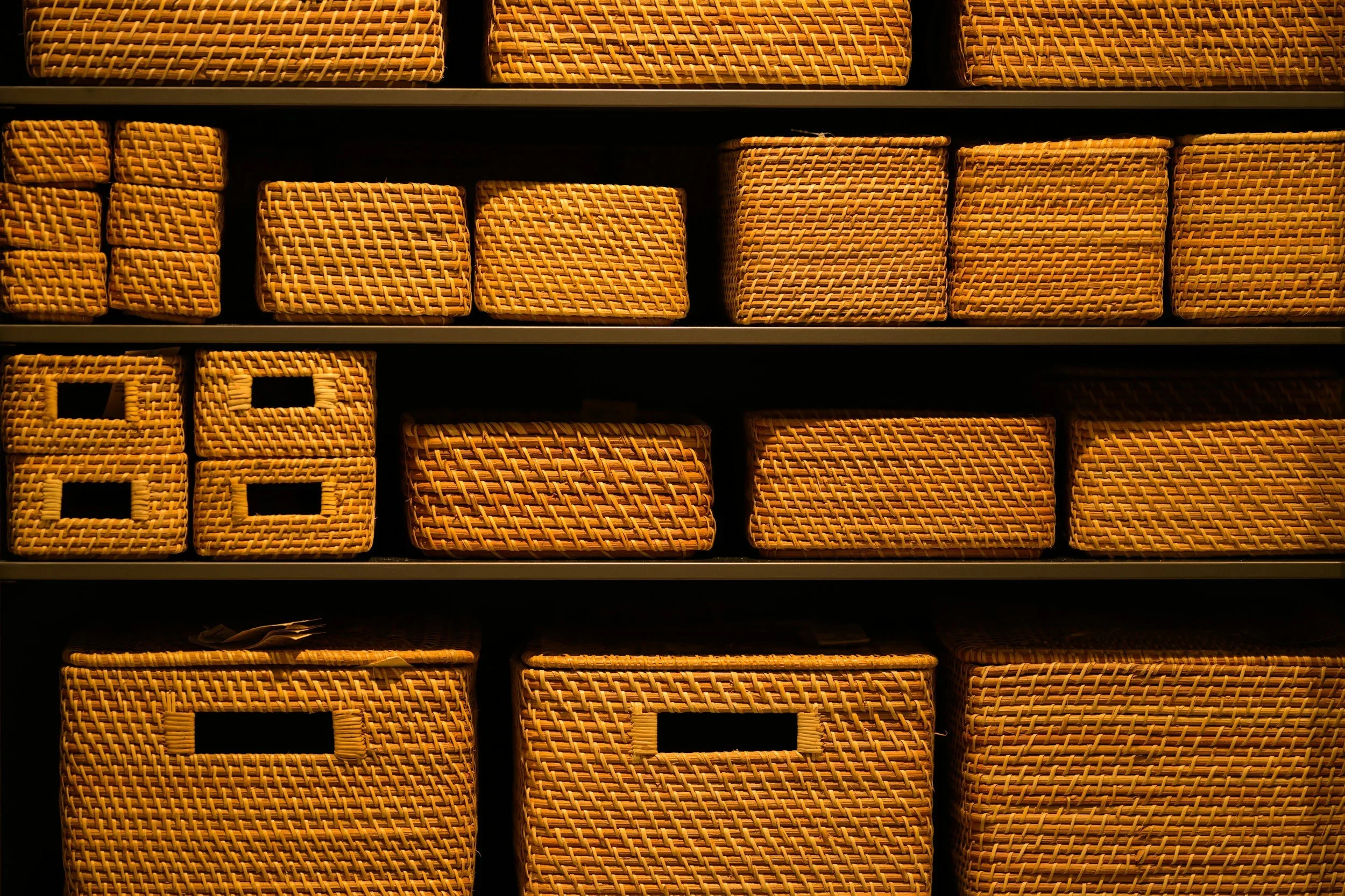 Rows of uniform woven rattan storage baskets on dark shelves in an organized pantry.
