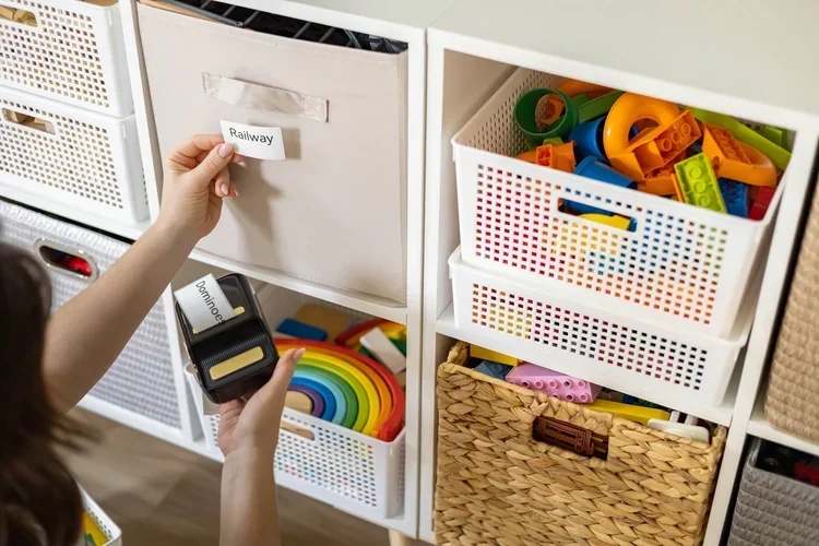 Hand applying a "Railway" label to a fabric bin in an organized toy storage unit.