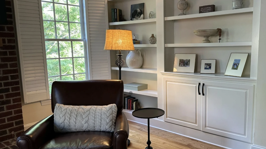 Organized white built-in bookshelves next to a cozy leather reading chair and floor lamp.