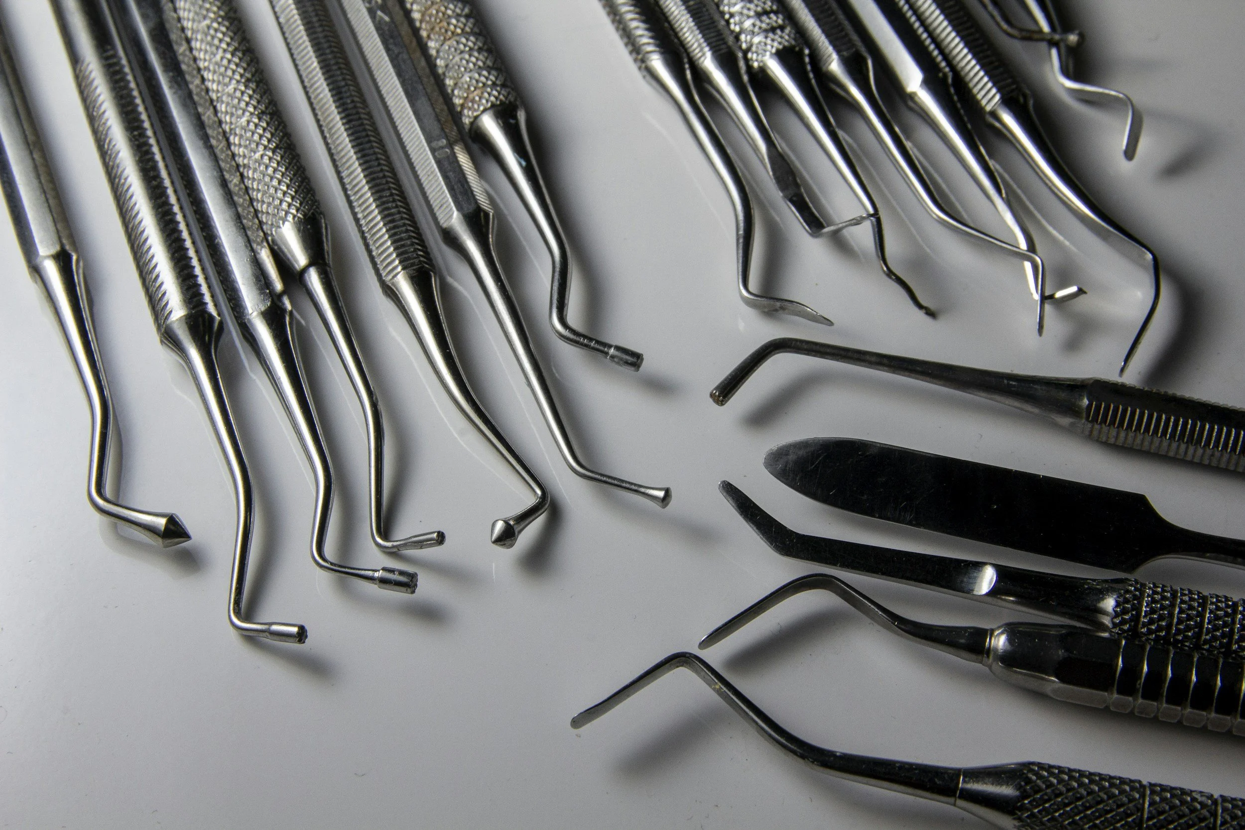 Collection of dental tools including dental picks, scaler, and probe laid out on a white surface.