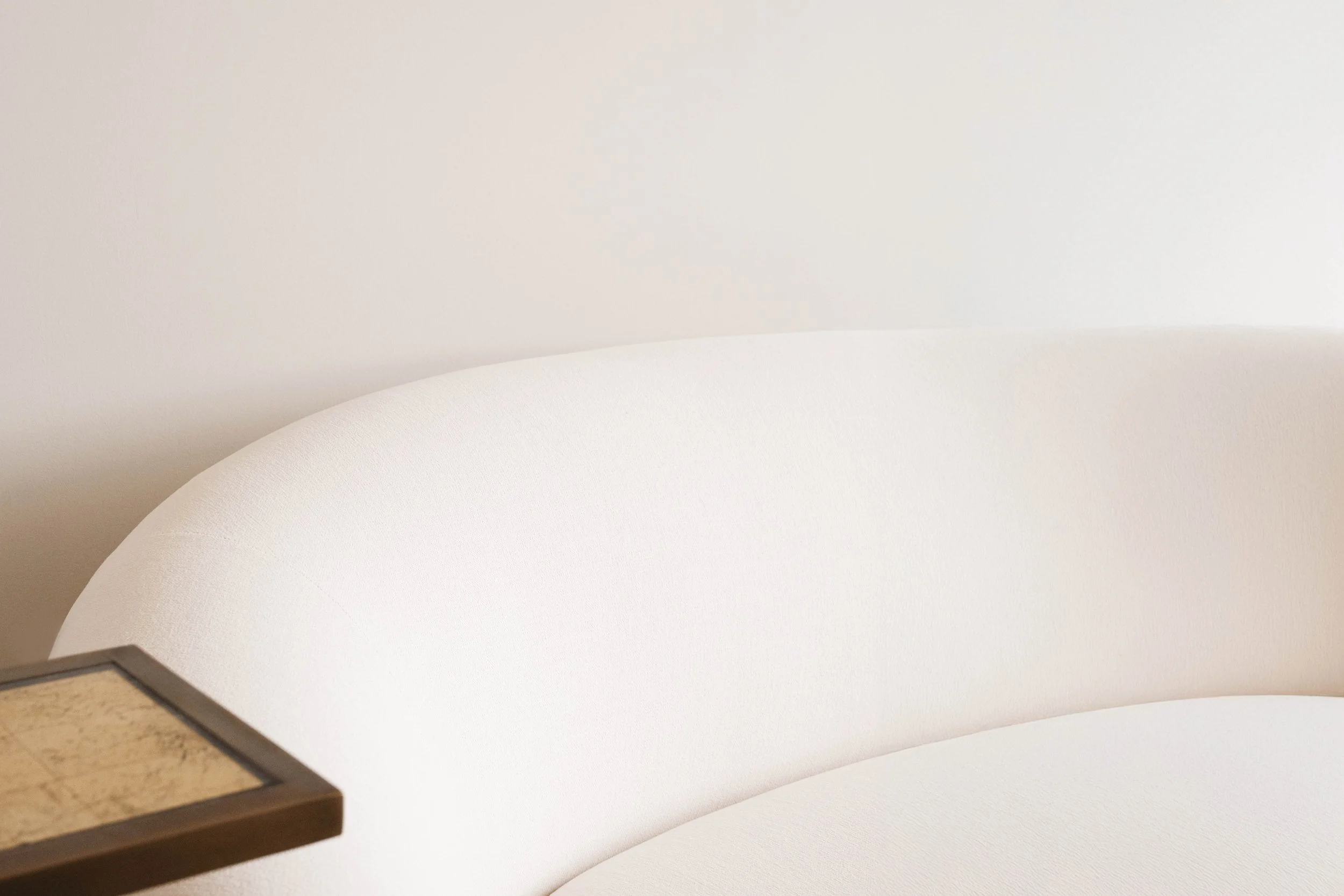 Close-up of a white modern sofa and a small wooden side table against a plain white wall.