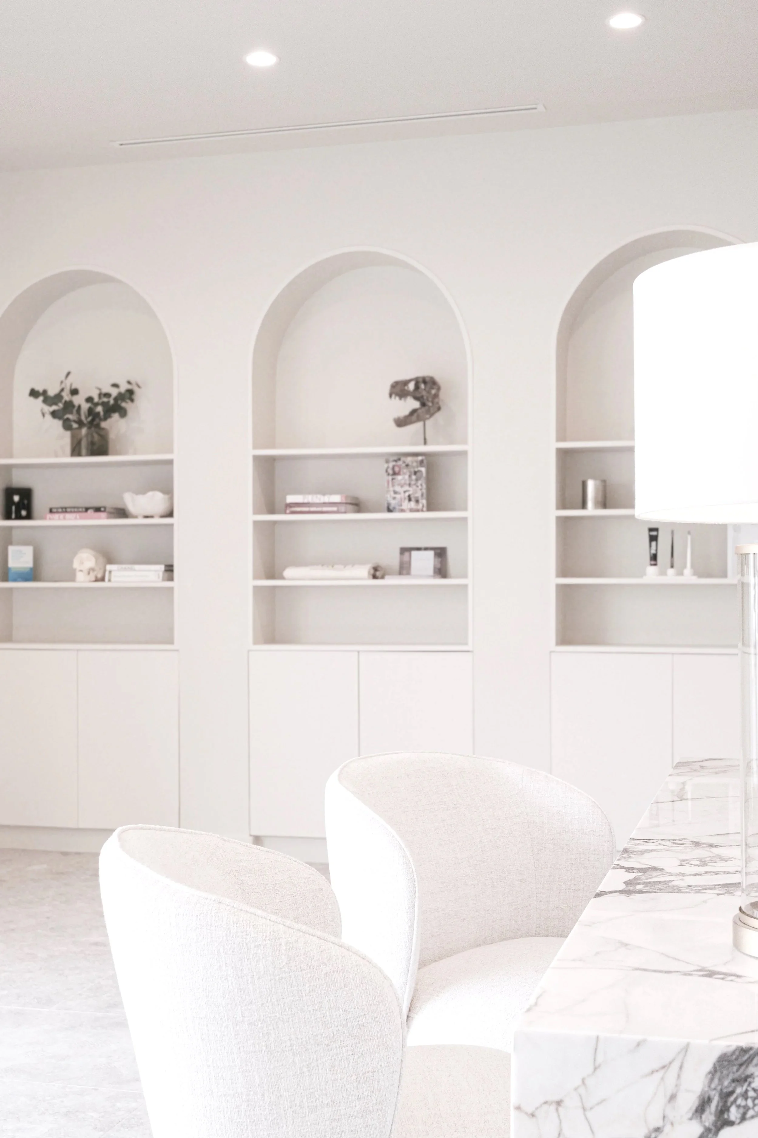 Minimalist white living room with built-in shelves, decorative items, and a marble countertop.