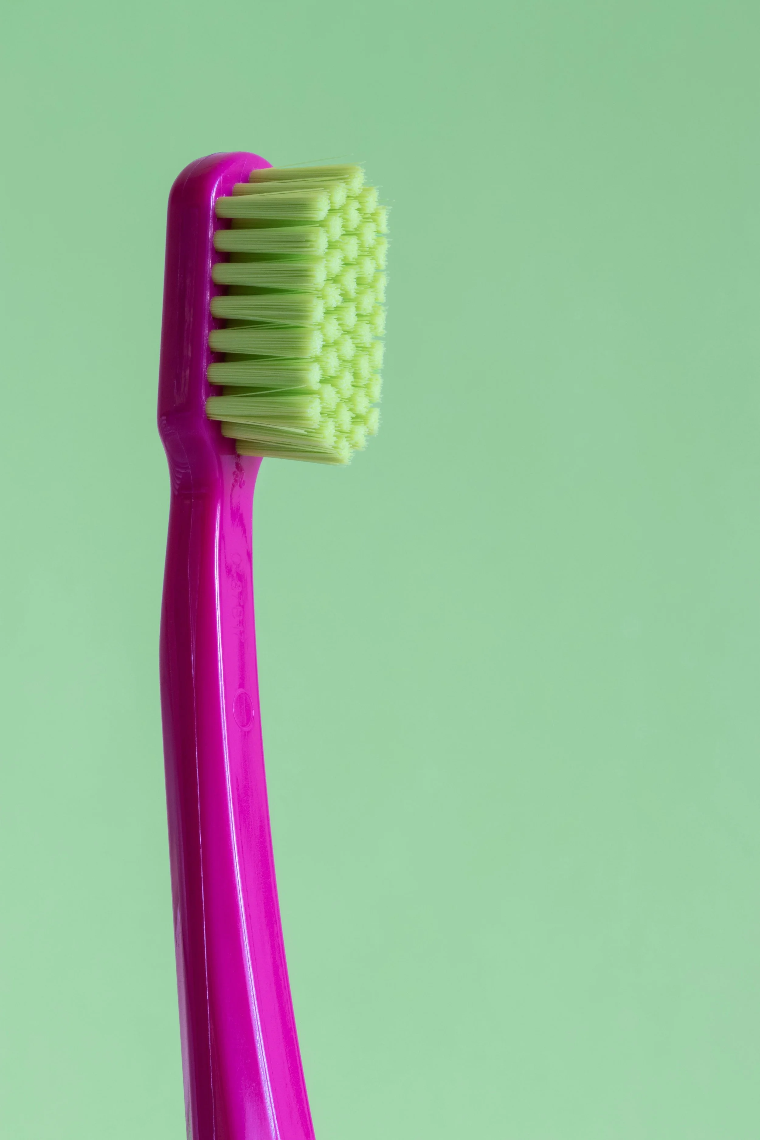 Close-up of a pink toothbrush with green bristles against a light green background.