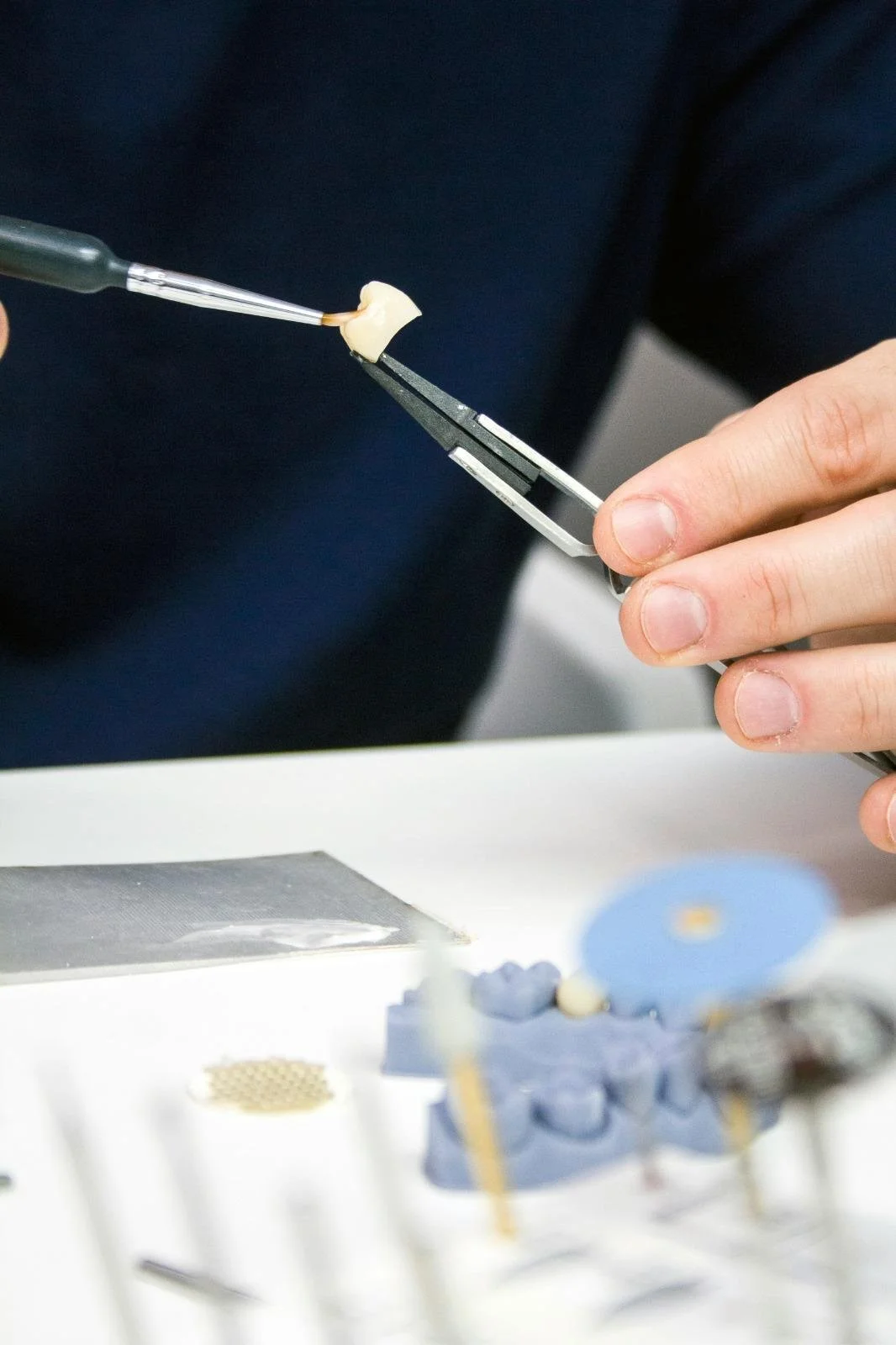 Dentist or dental technician handling a dental prosthetic or crown with precision tools during dental lab work.