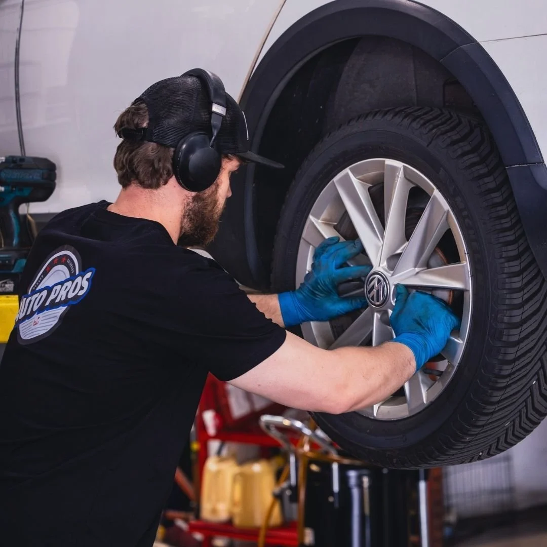 A gloved mechanic in a black hoodie and mesh cap using a tool on a car engine.