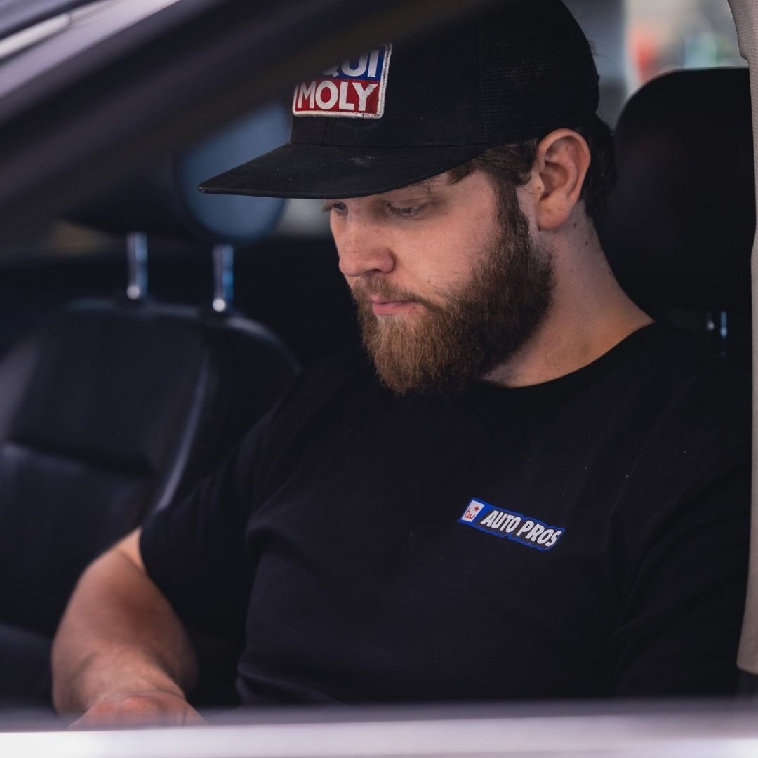 A bearded man in an Auto Pros t-shirt and a Liqui Moly cap looking down intently.