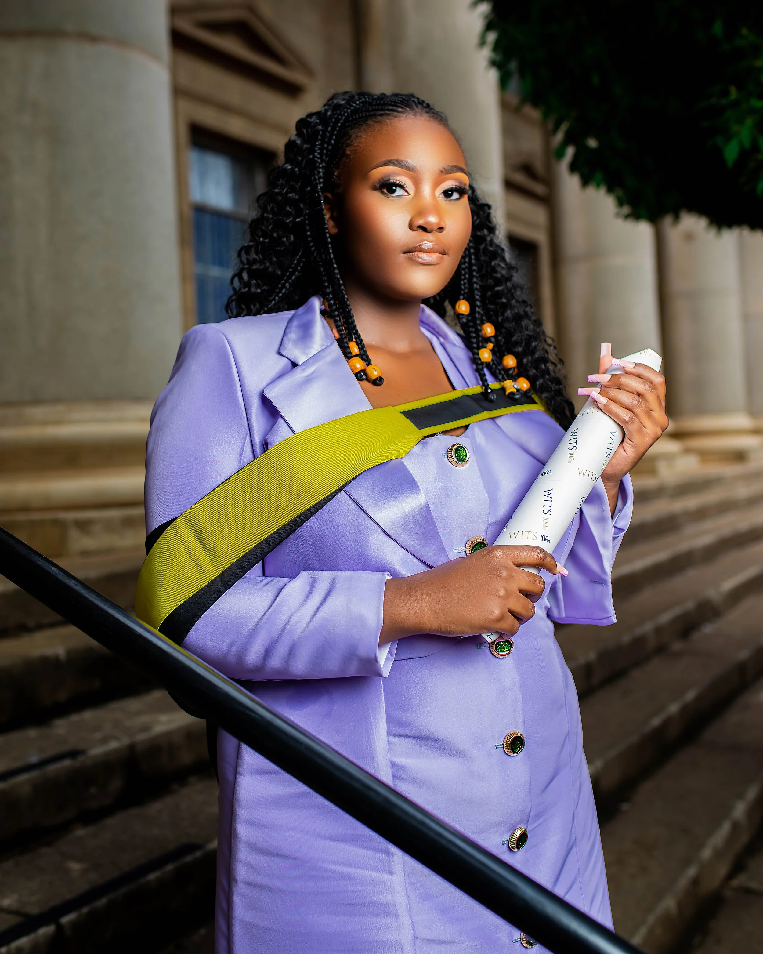 A person in a lilac outfit holding a scroll, standing on stone steps. Photographed at Wits University, Johannesburg. 