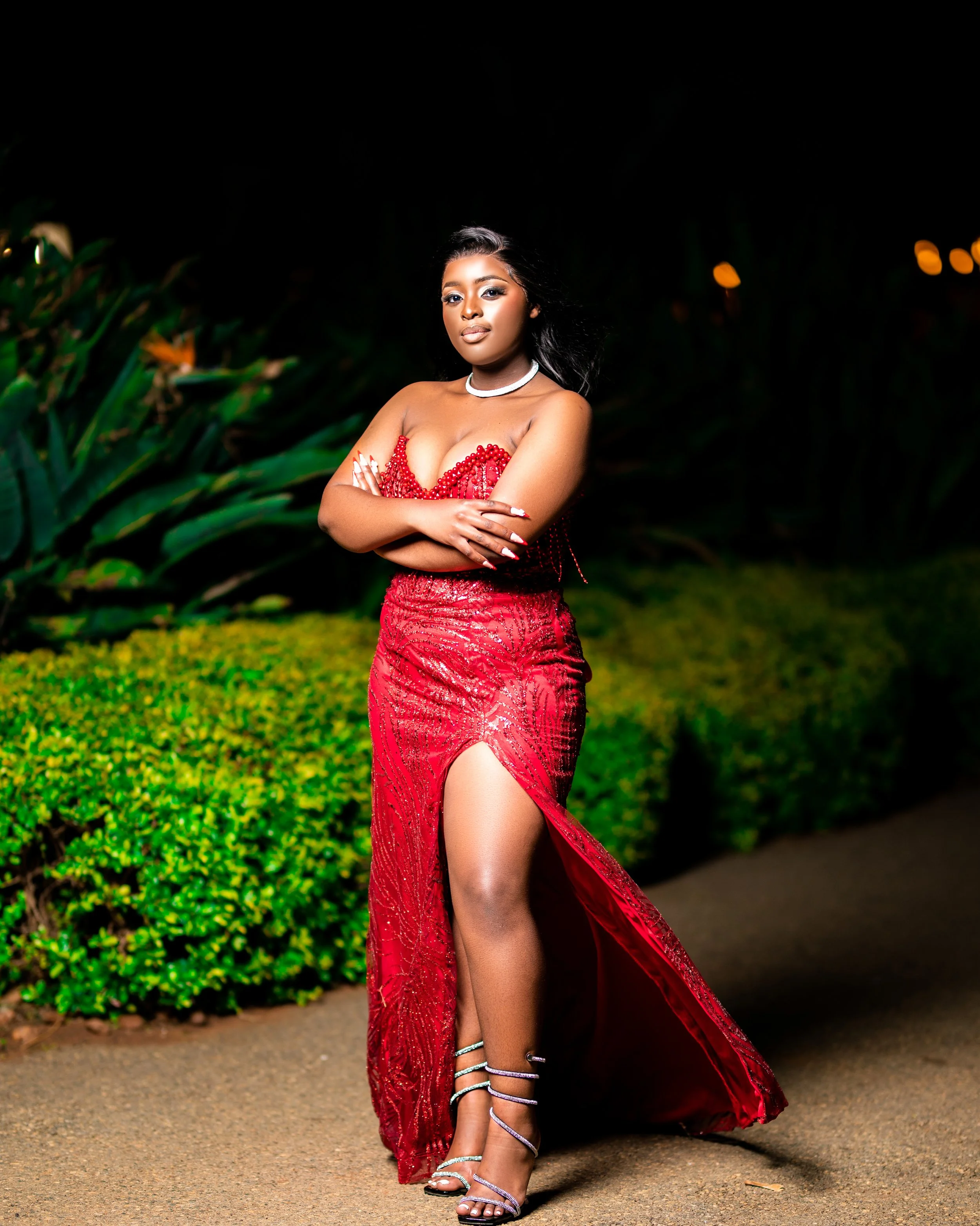Person in a red dress posing on a pathway with greenery background at night. Photographed in Johannesburg, South Africa.