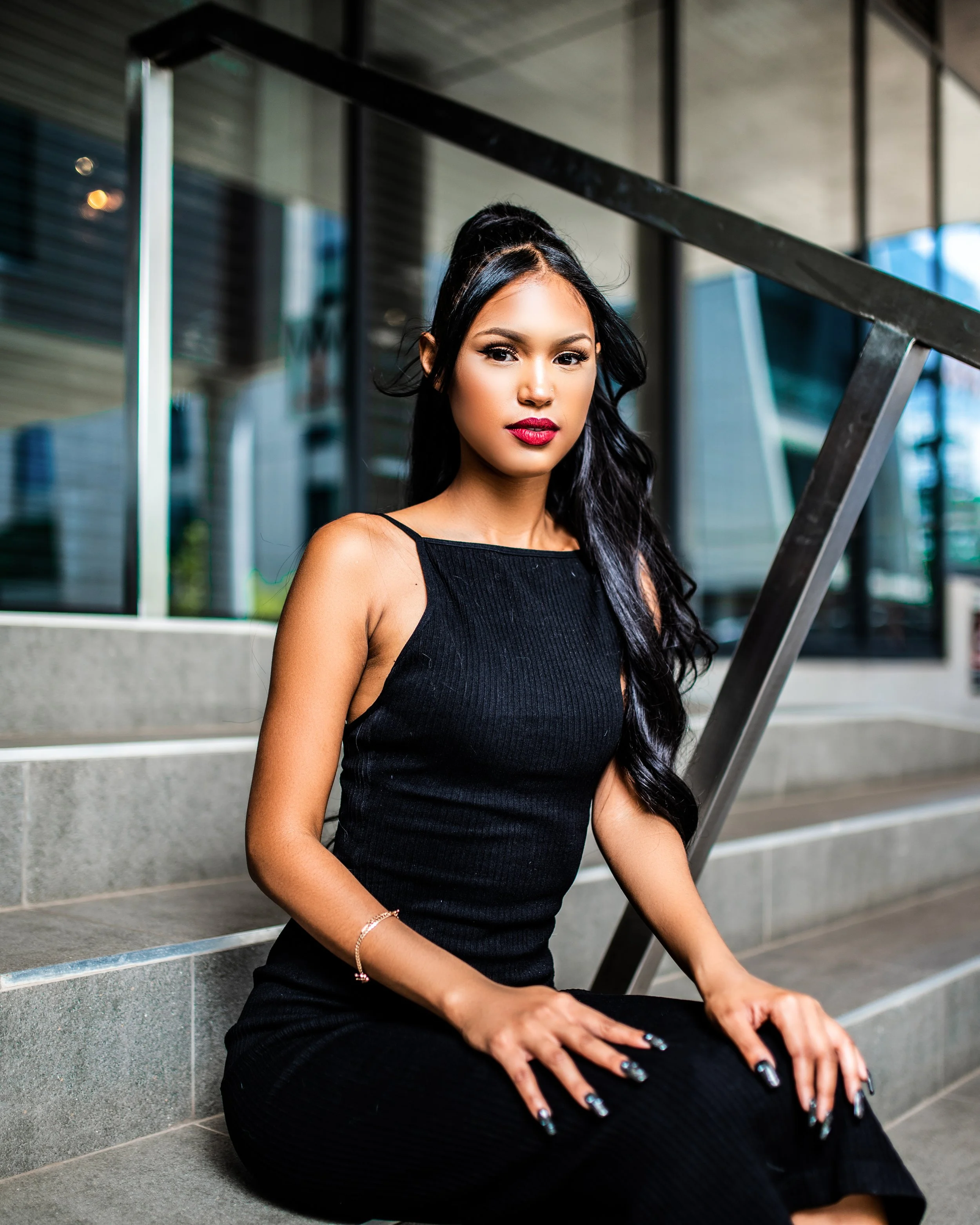 Woman in a black dress sitting on steps, urban background. Photographed in Rosebank, South Africa.