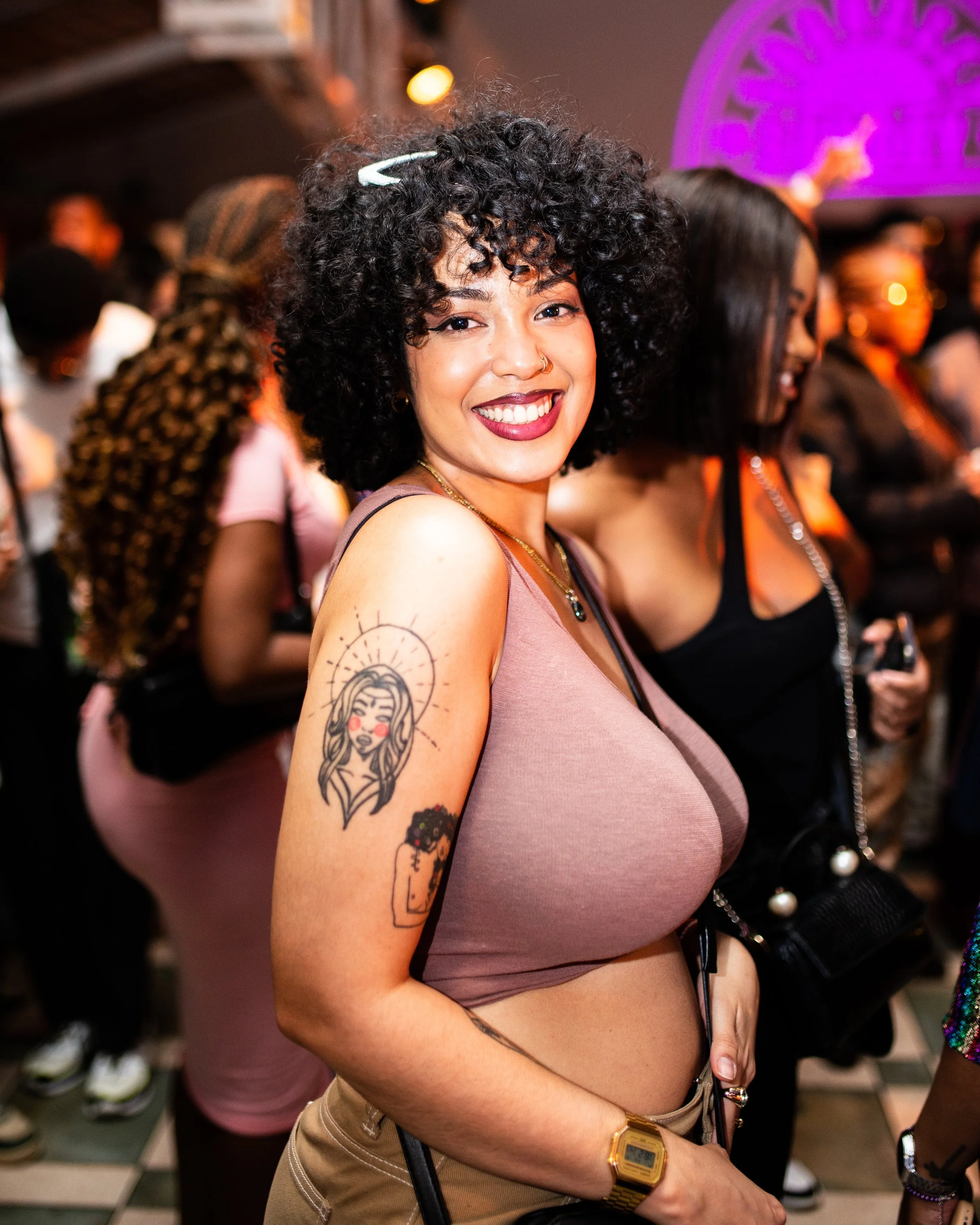 Smiling woman at a social event, wearing a brown top and displaying a tattoo on her arm. Photographed in Johannesburg, South Africa.
