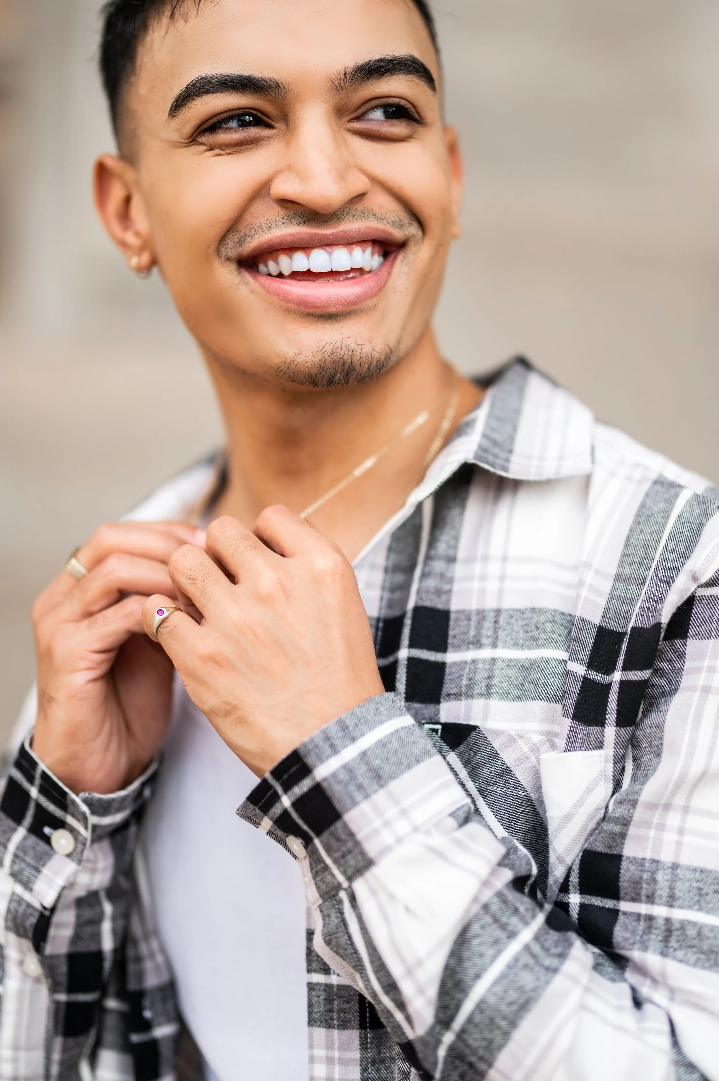 Man smiling, wearing a plaid shirt and holding a necklace.  Photographed in Sandton, Johannesburg. 