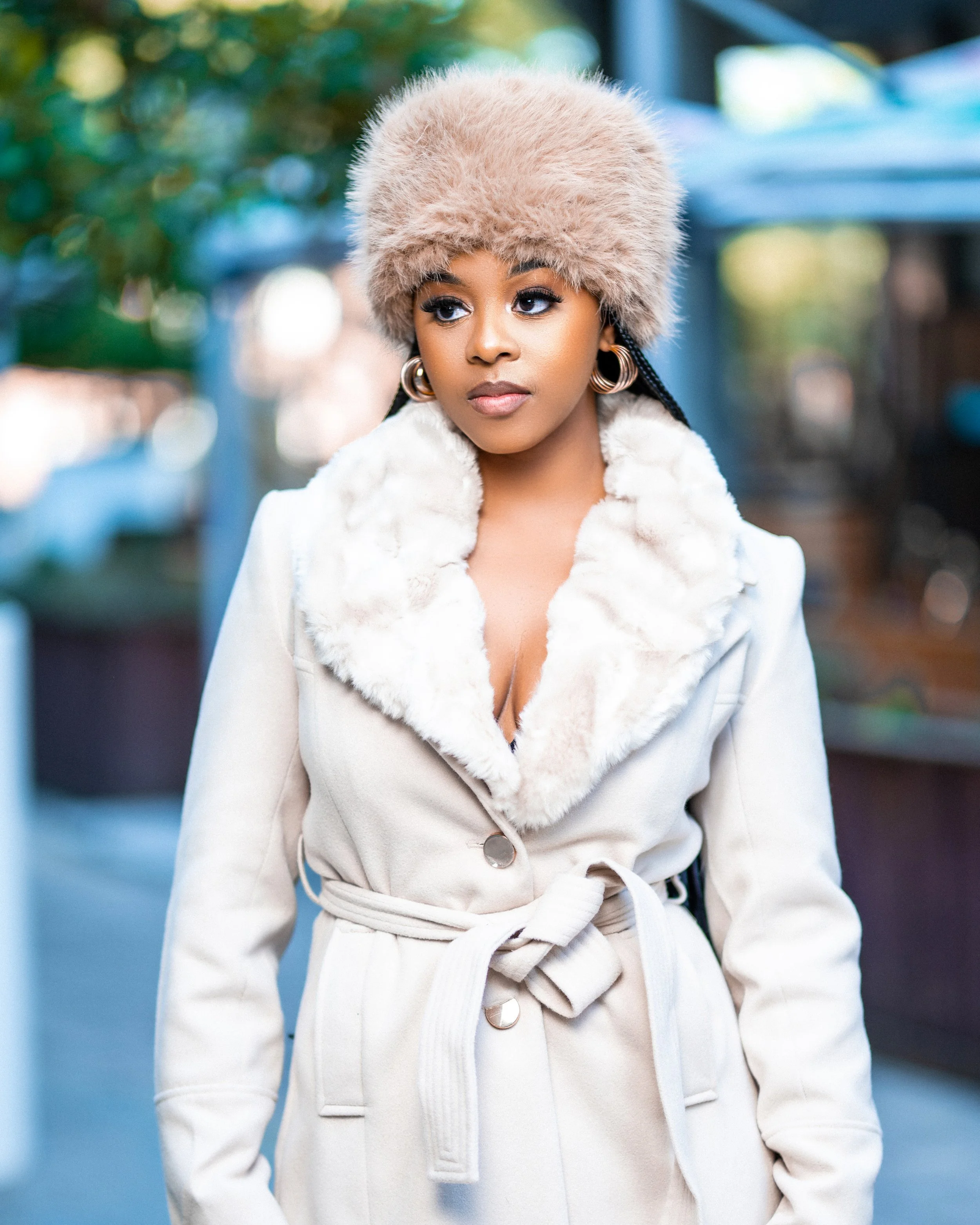 Woman wearing a fur hat and belted fur-lined coat in a city setting. Photographed in Rosebank, Johannesburg. 