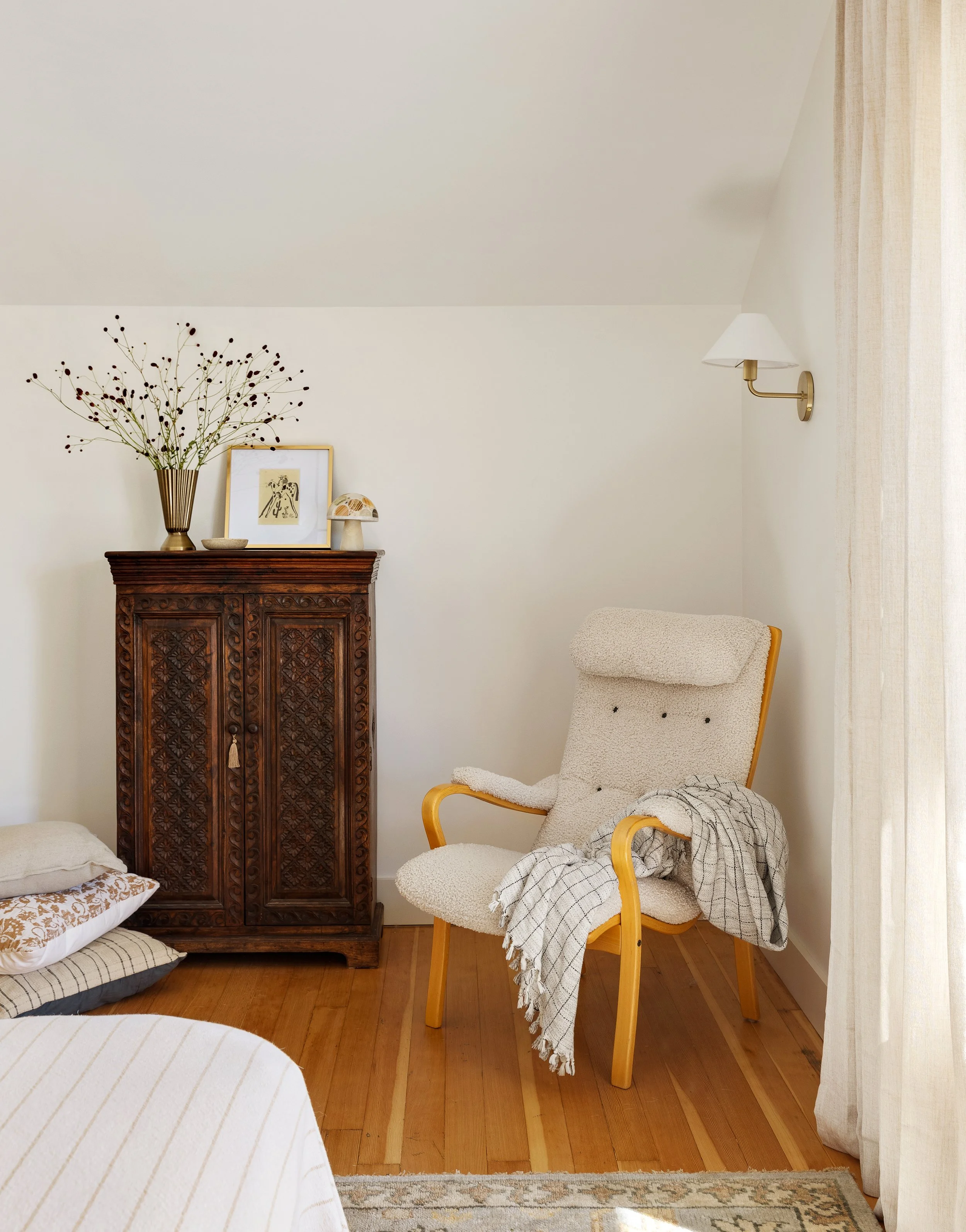 A cozy bedroom corner designed by Portland interior designer Anna Reinhard Interiors with a vintage cabinet and lounge chair.
