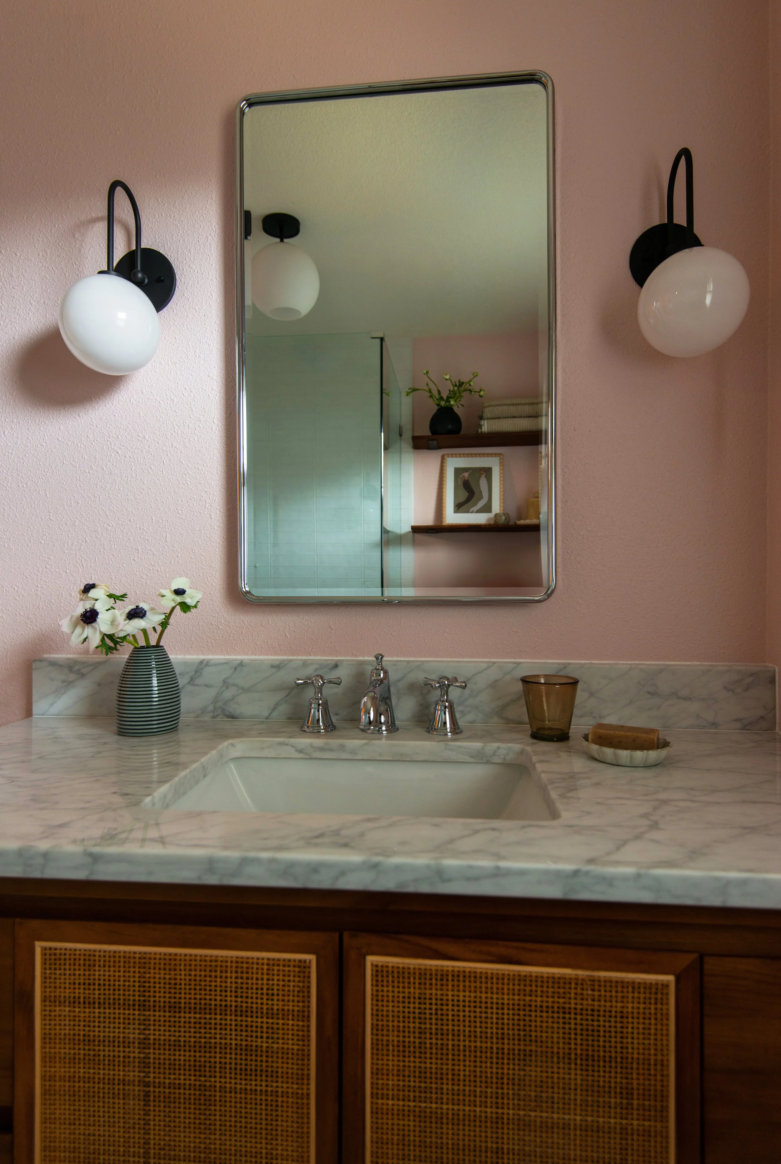 Vintage-inspired bathroom renovation by Portland interior designer Anna Reinhard Interiors. Blush paint, black sconces, carrara marble vanity with cane detailing. Rejuvenation medicine cabinet.